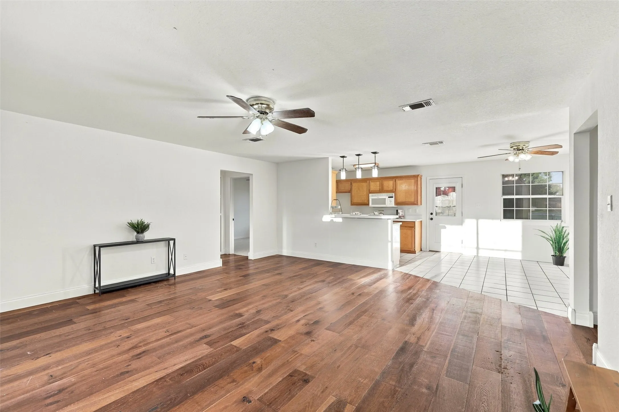 Living Area: Expansive living space with warm wood floors, a ceiling fan, and an open view of the kitchen's breakfast bar.