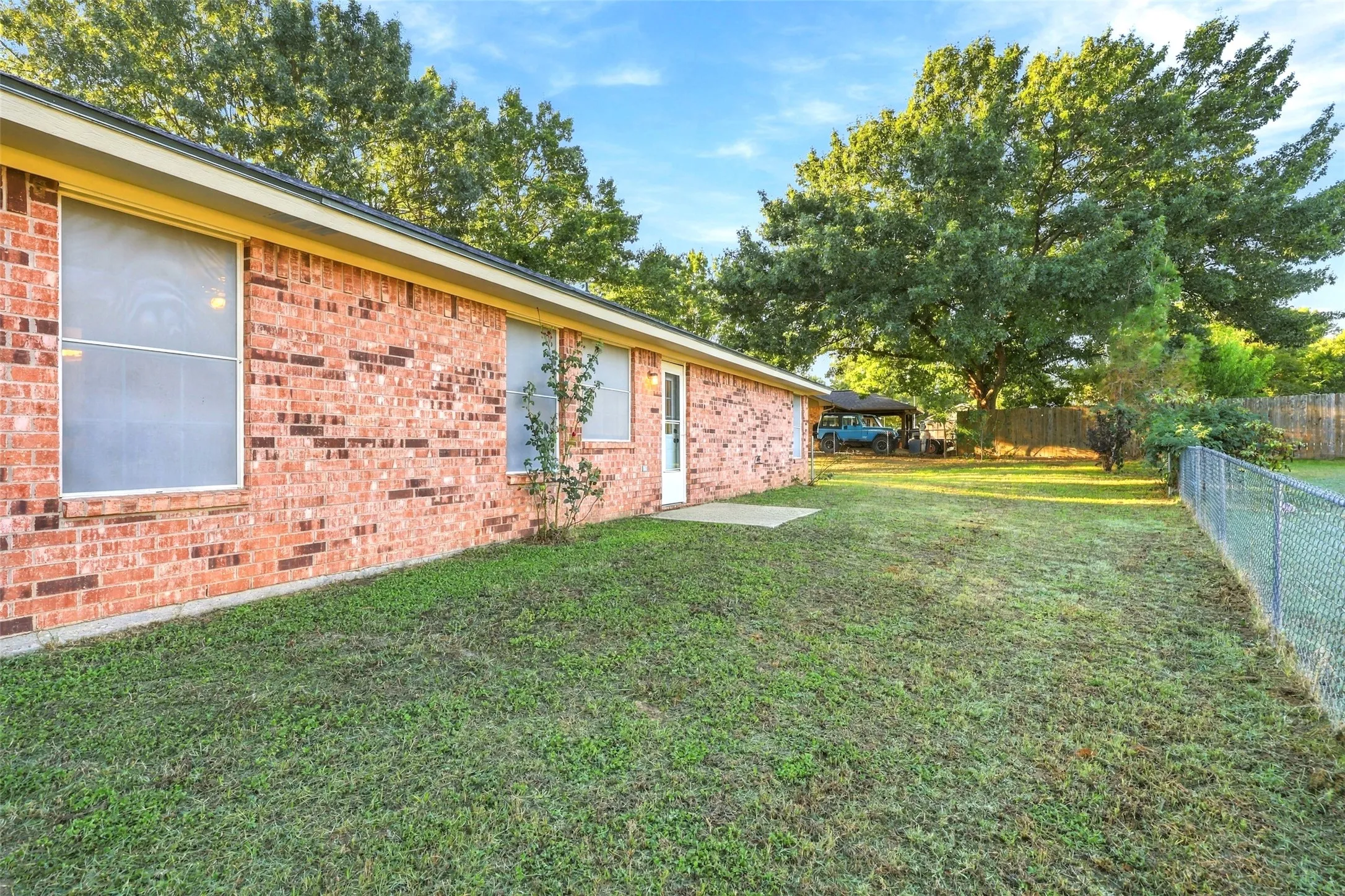 Side Yard – Fenced grassy area with brick exterior, rear entry, and mature shade trees.
