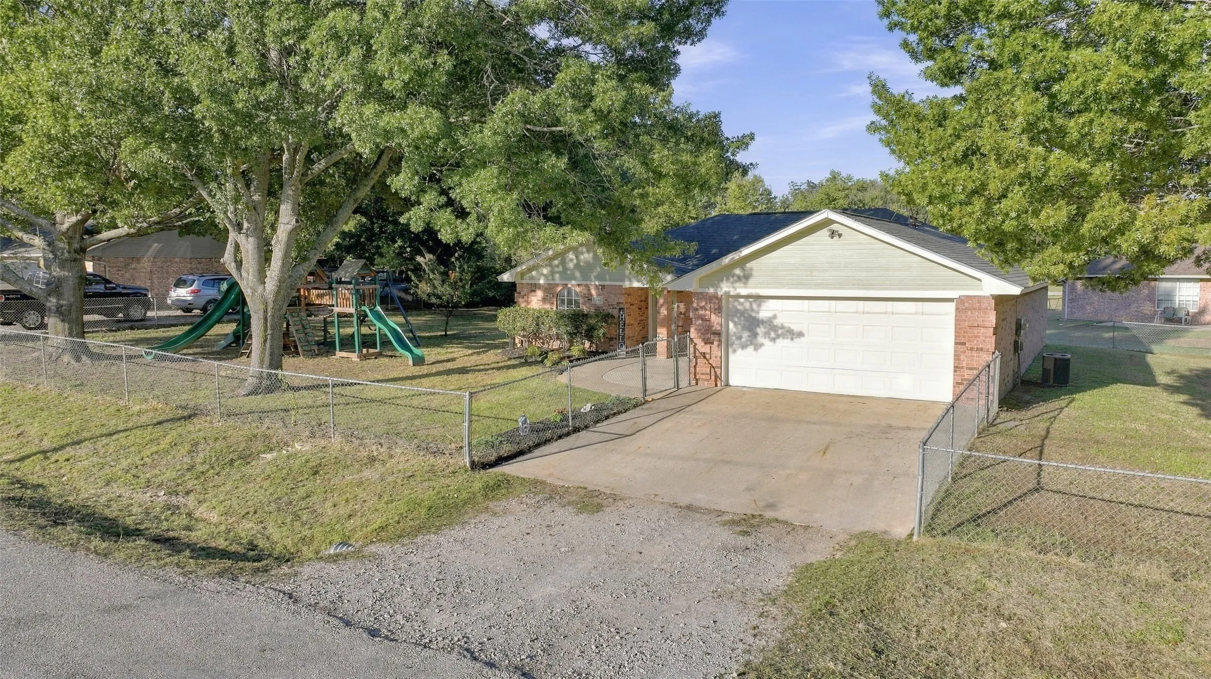 Aerial Front View – Single-story brick home with attached two-car garage and fenced front yard.
