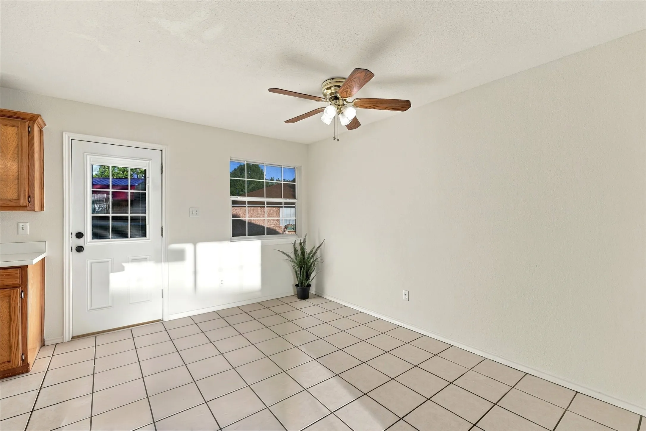 Dining Area: Sunlit dining space featuring tile flooring, a ceiling fan, and a window overlooking the outdoor area.