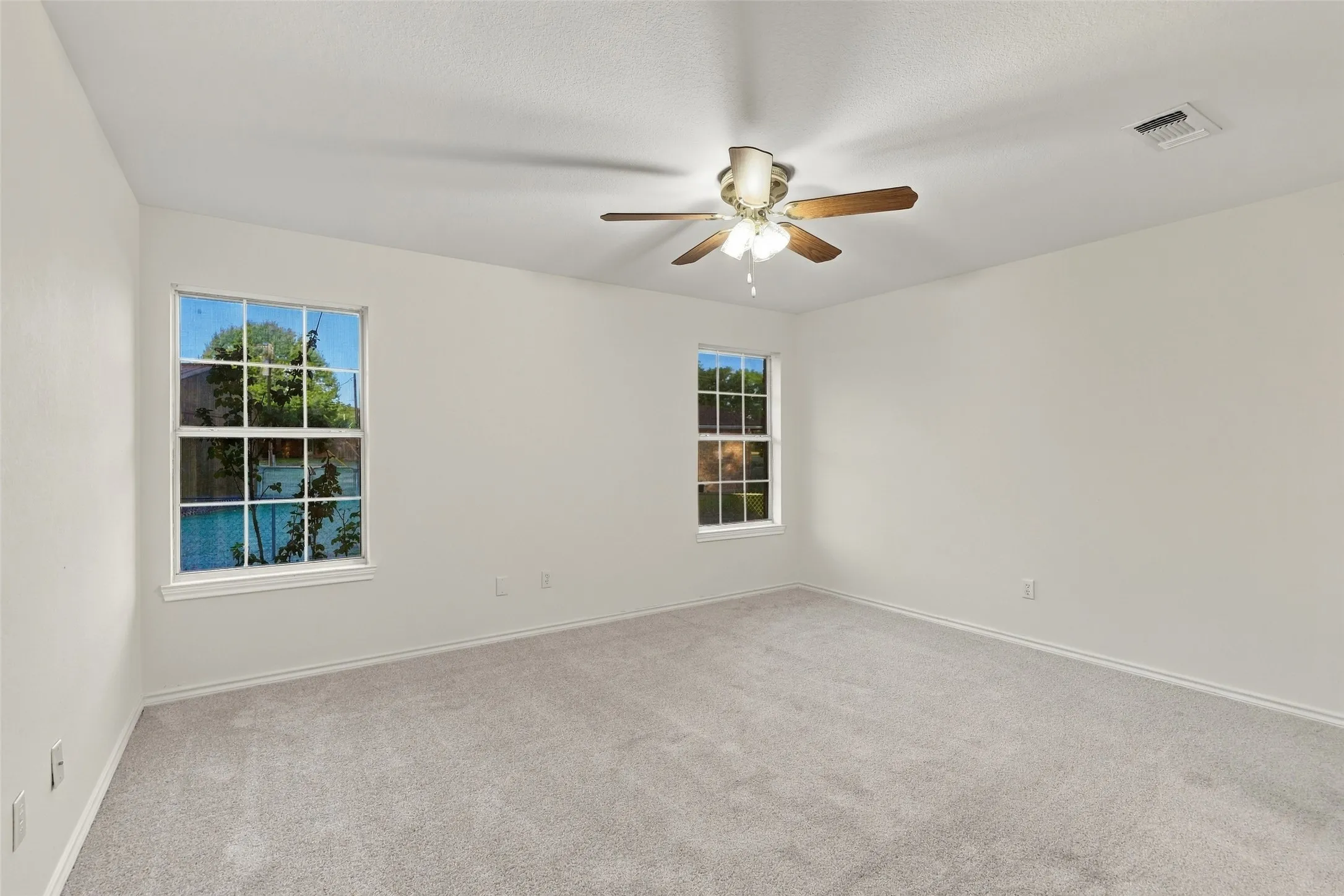 Bedroom: Spacious carpeted bedroom with neutral finishes, two windows providing natural light, and a ceiling fan.