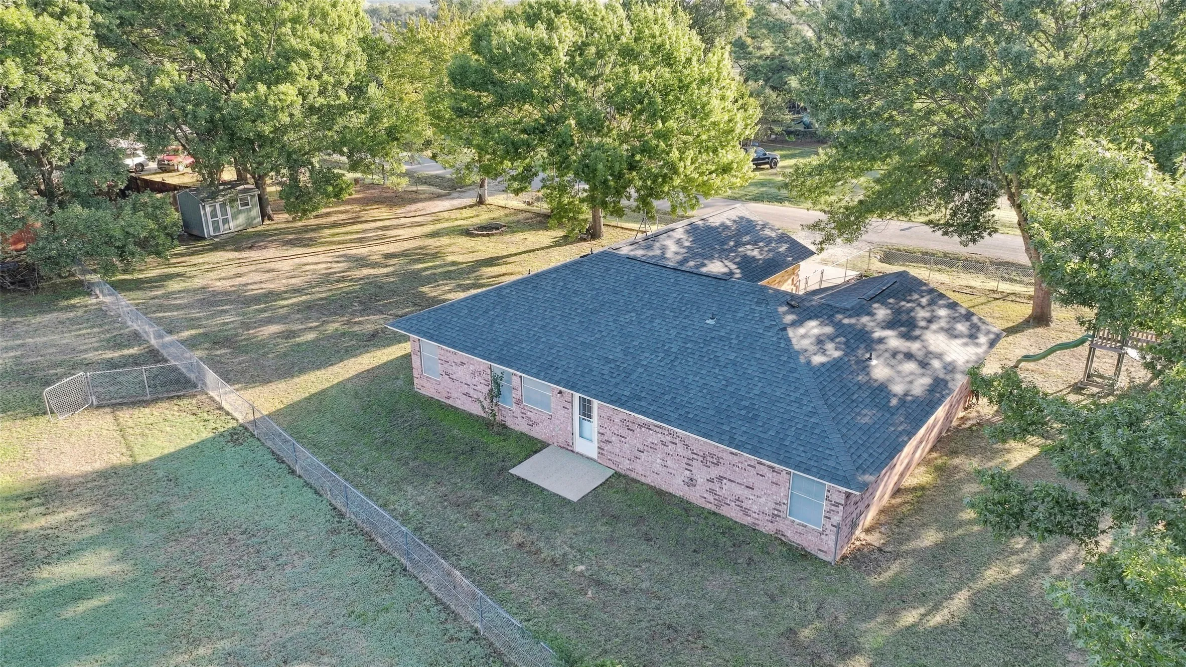 Aerial Rear View – Elevated perspective showcases the spacious lot, fenced yard, and mature trees.