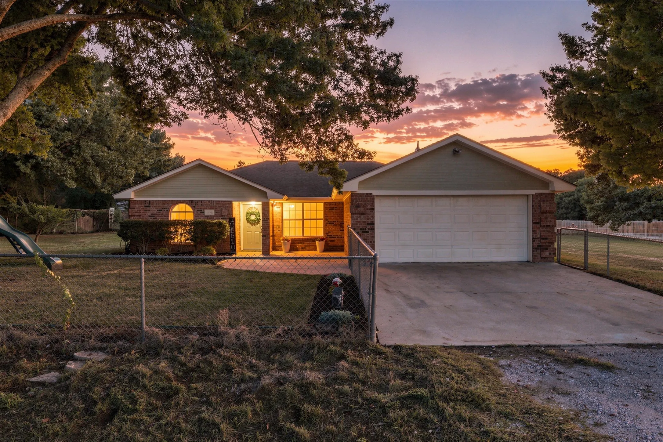 Front Exterior – Single-story brick home with mature oak trees, fenced yard, and sunset views.