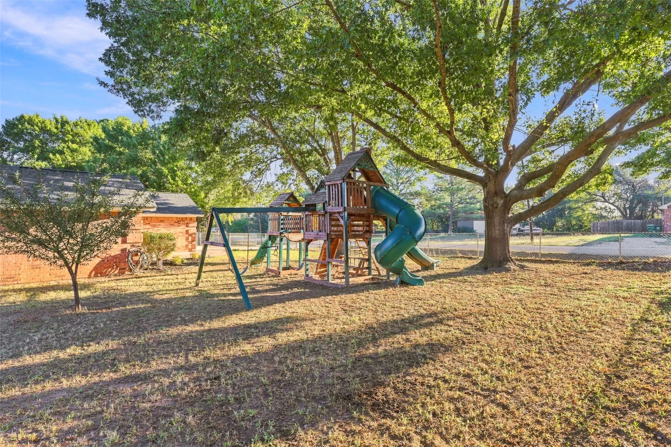 Outdoor Space – Expansive shaded yard with mature oak trees and wooden playground.