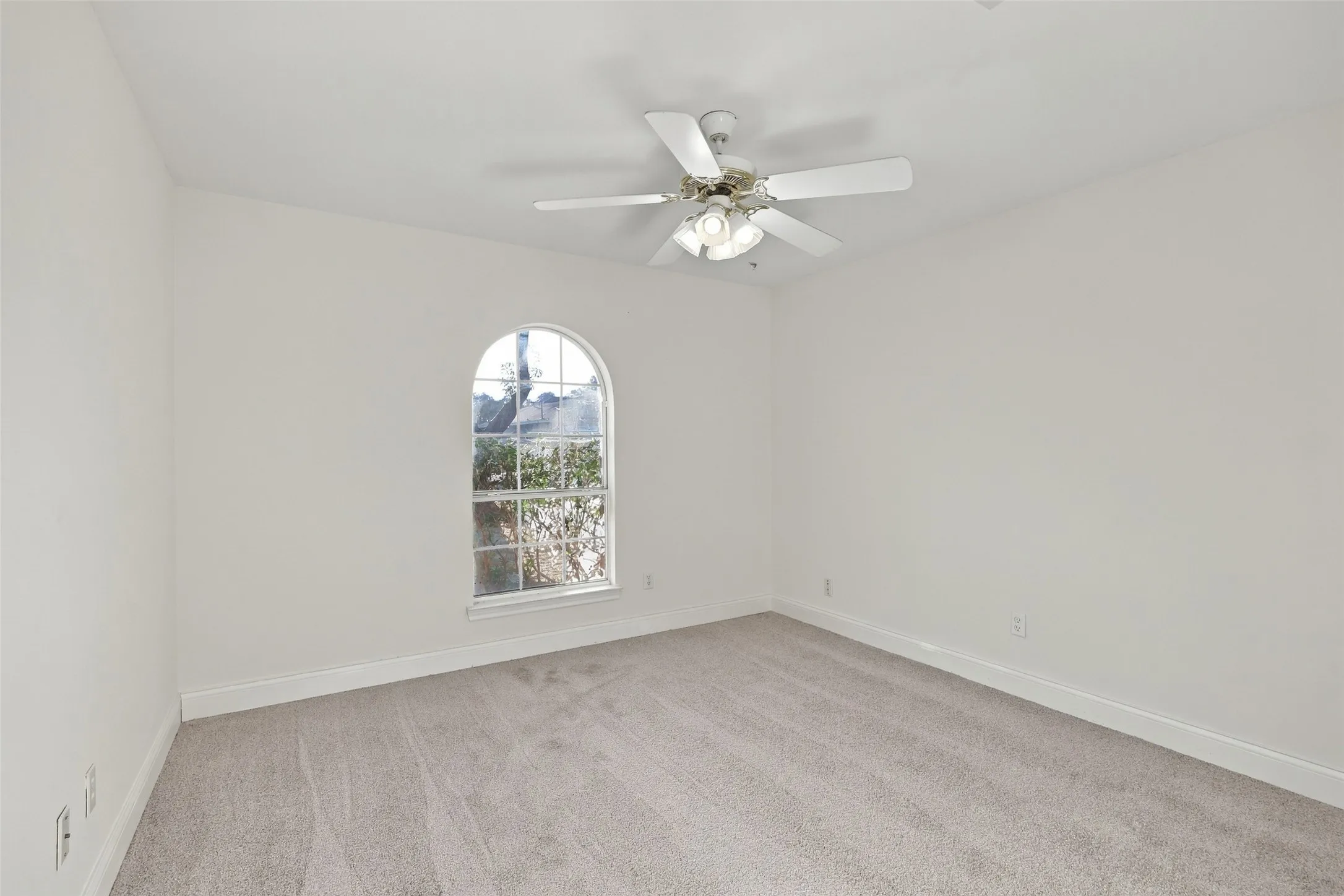 Bedroom: Light-filled bedroom showcasing an arched window, soft carpeting, and a ceiling fan with integrated lighting.