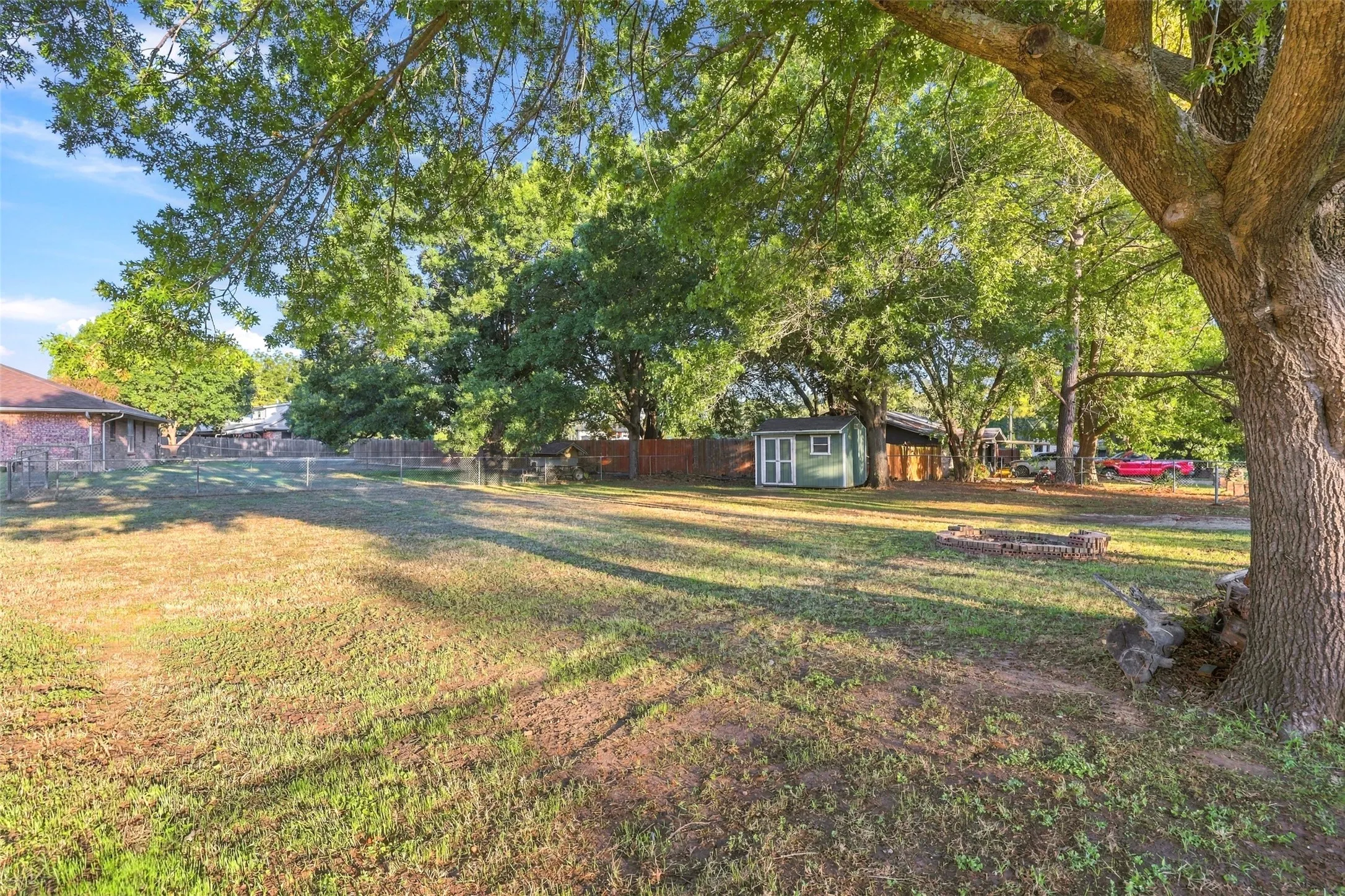 Backyard – Spacious fenced yard featuring mature oak trees and a detached storage shed.