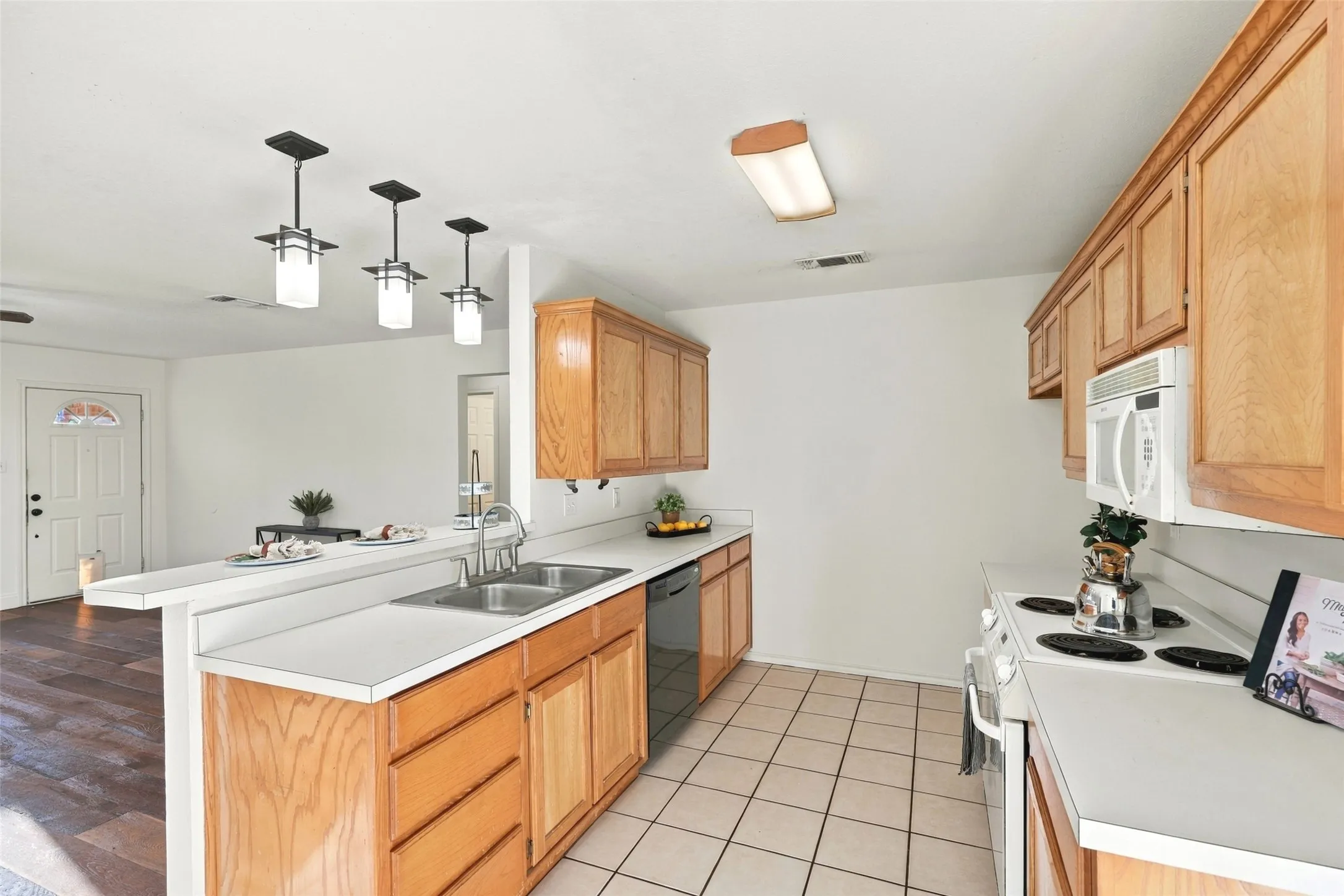 Kitchen: Natural wood cabinetry, white countertops, a double-basin sink, and pendant lighting above the breakfast bar.