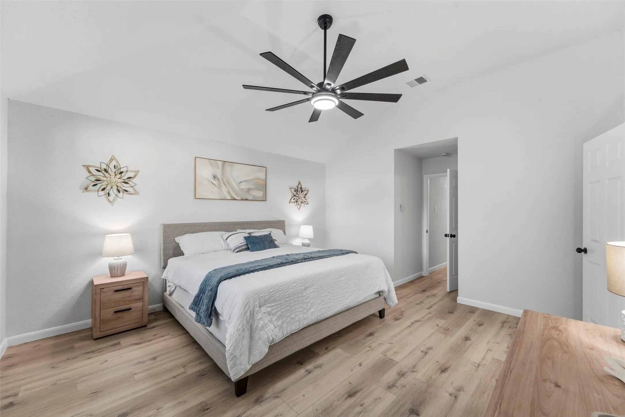 Vaulted ceiling with a contemporary ceiling fan, wood-finish flooring, and white paneled door