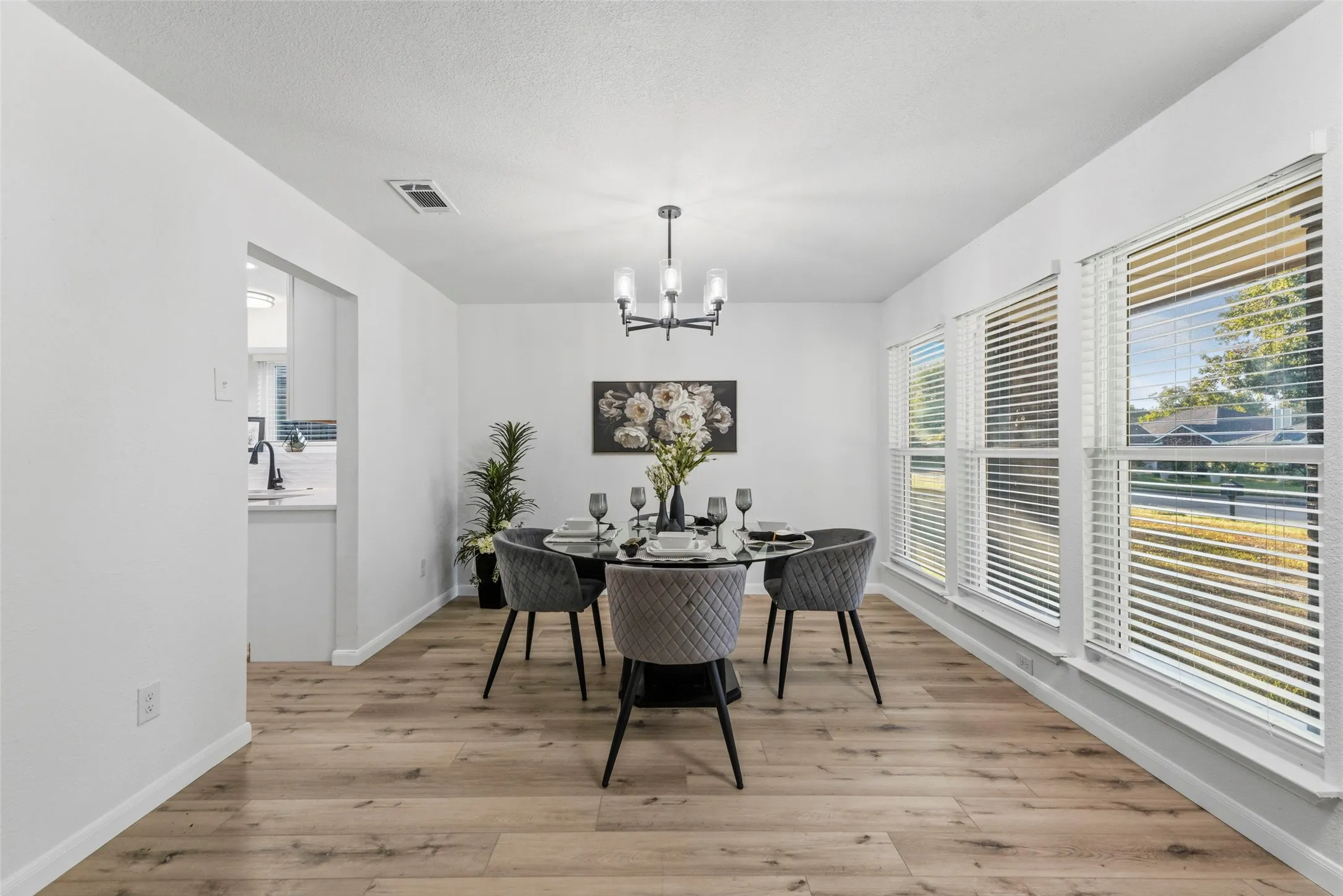 Bright dining area featuring multiple large windows, wood-finish flooring, and a contemporary chandelier