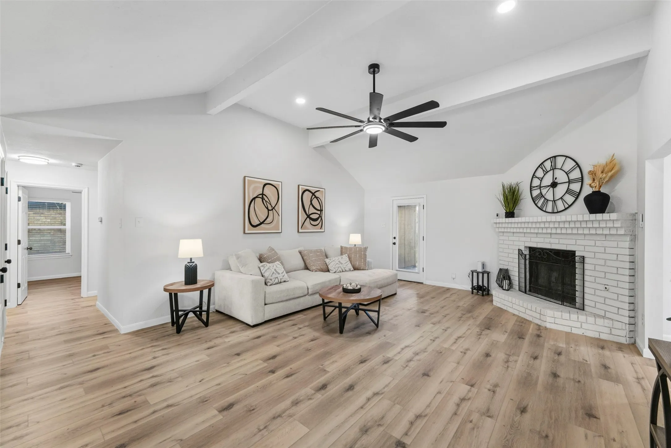 Vaulted ceilings, wood-finish flooring, a white brick fireplace, a ceiling fan, and recessed lighting