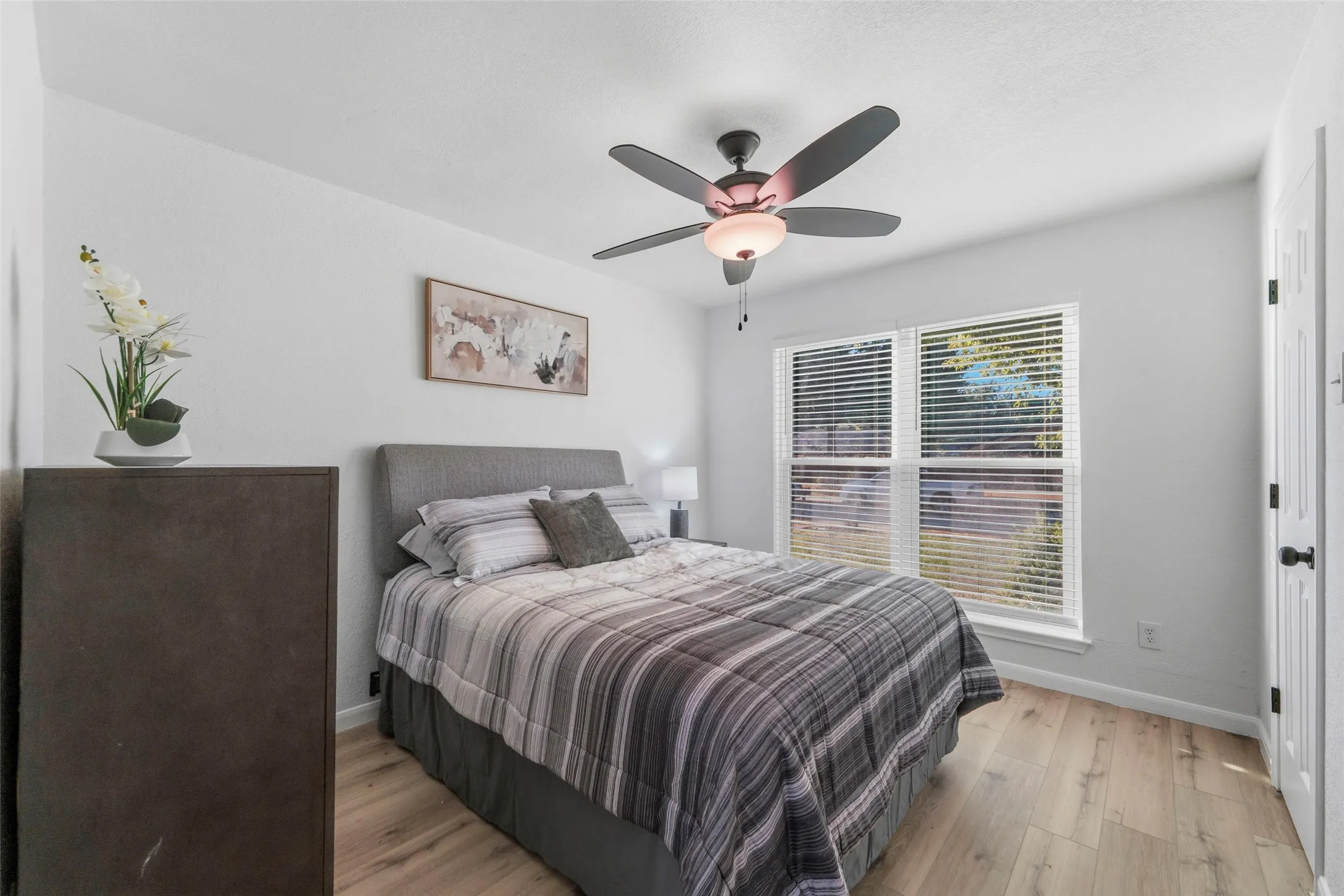 Bright room with wood-finish flooring, a ceiling fan with integrated lighting, and a window featuring blinds