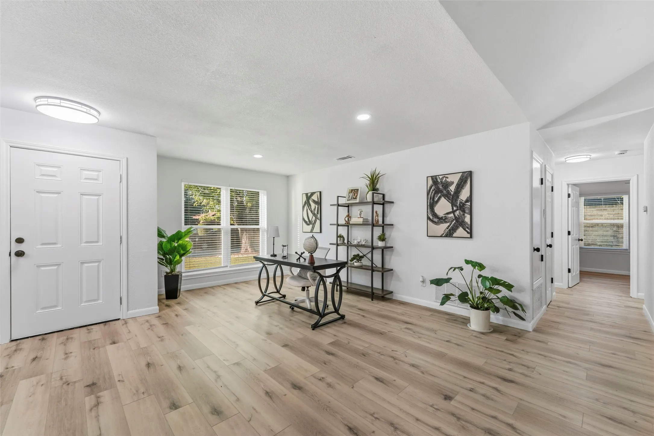 Recessed and flush-mount ceiling lighting illuminate an open-concept room with wood-finish flooring, white walls, and a multi-pane window