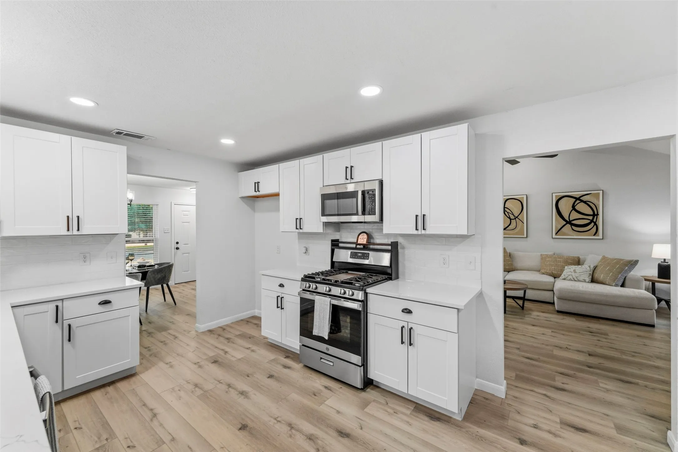 Modern kitchen featuring white shaker cabinets, white countertops, stainless steel appliances, wood-finish flooring, and recessed lighting