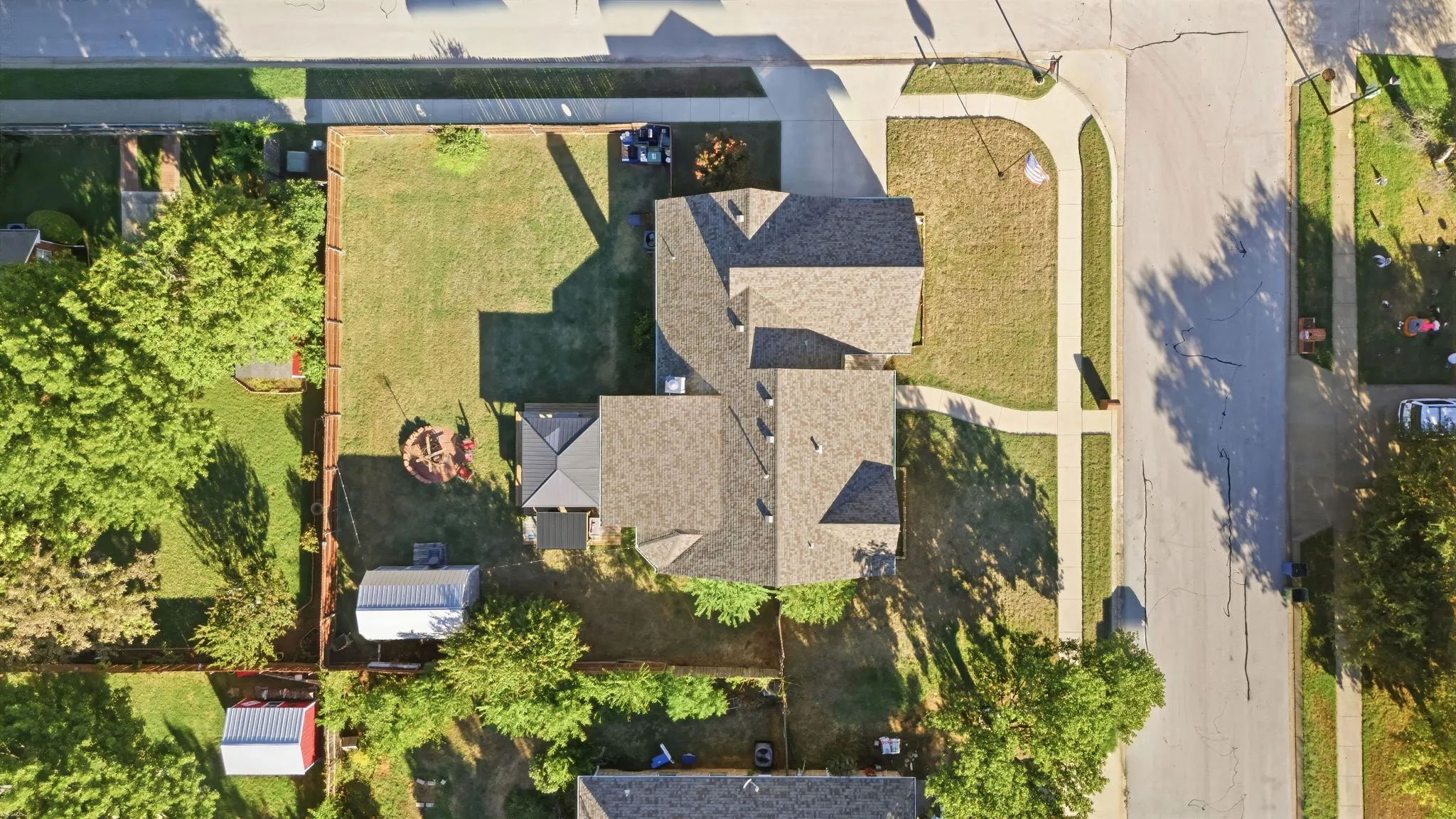 Aerial view showcasing a multi-level residence with complex architectural design, featuring multiple roof peaks and dormers, mature landscaping with established trees throughout the grounds, and a spacious lot with manicured lawn areas and defined hardscaping elements
