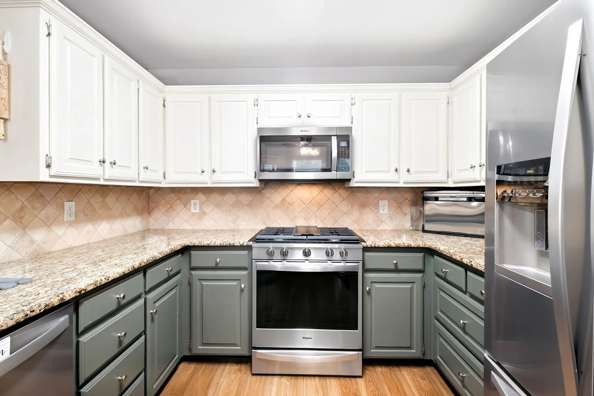 Kitchen featuring two-tone cabinetry, granite countertops, tile backsplash, and stainless steel appliances