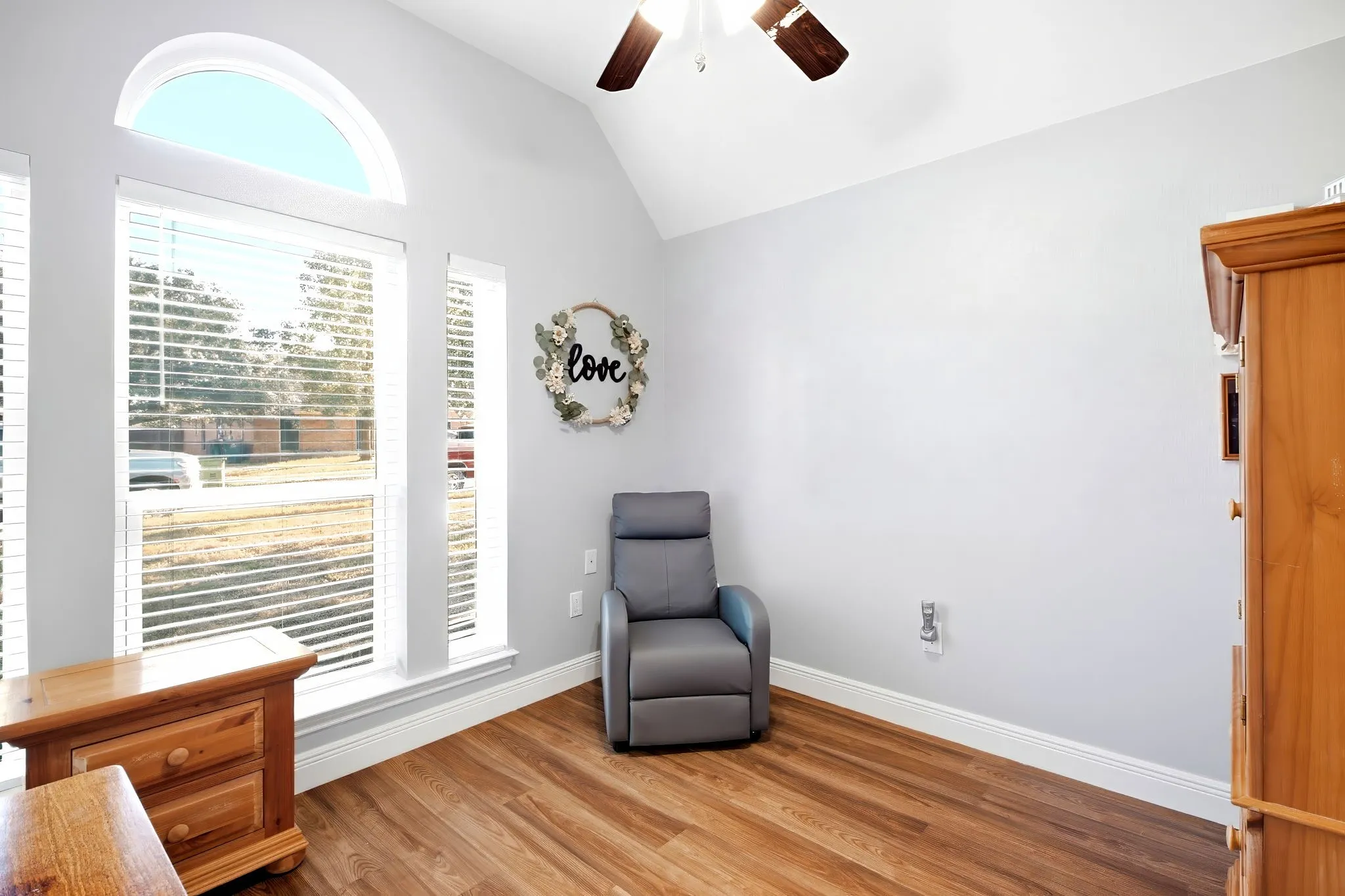 Vaulted ceiling with a ceiling fan, multiple windows including an arched transom, wood-finish flooring, and white trim