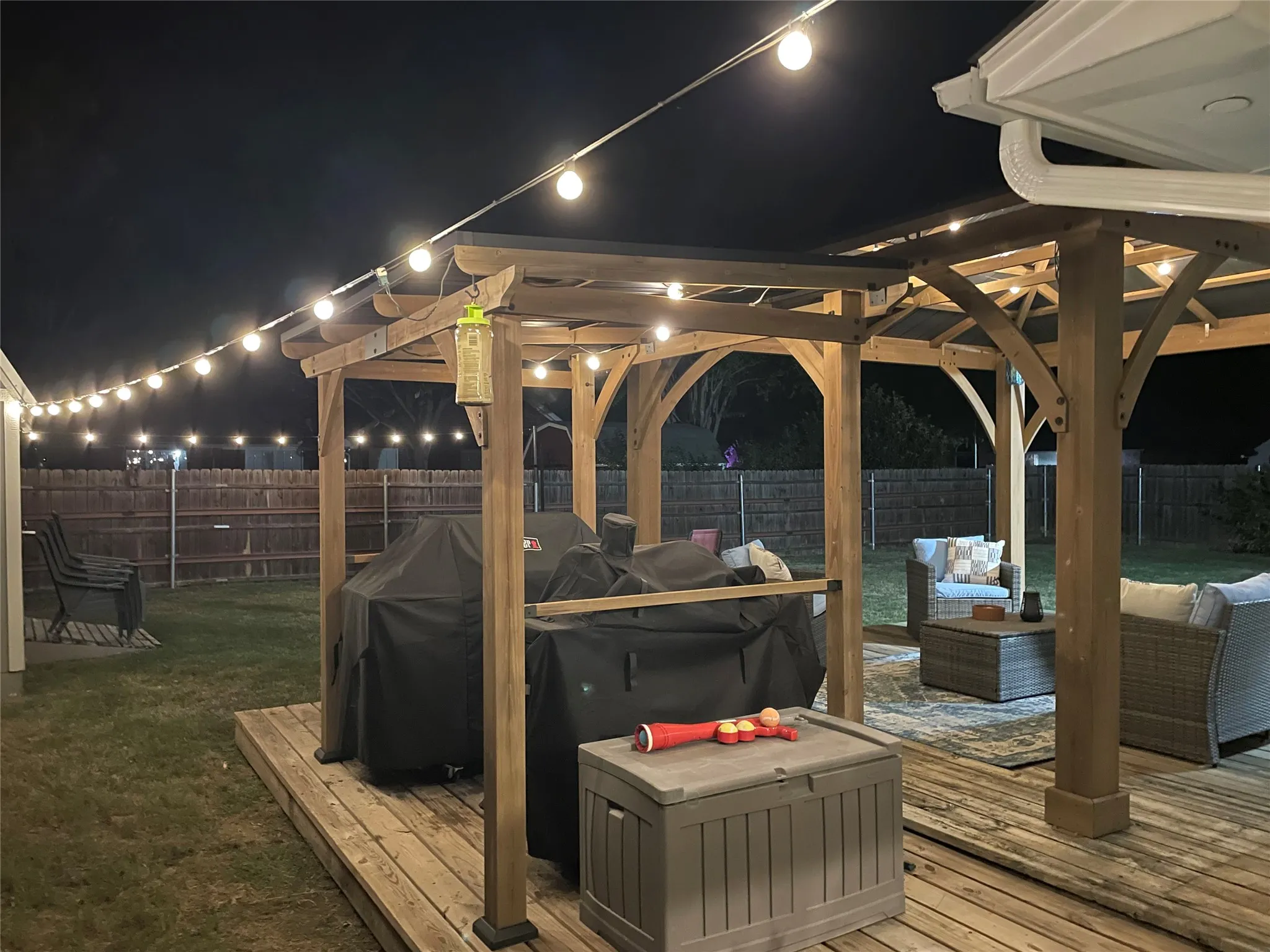 Expansive backyard deck featuring a wooden pergola, string lighting, and a privacy fence