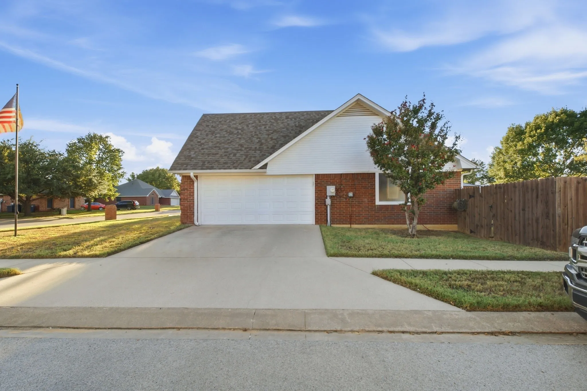 Brick and siding exterior with a pitched roof, attached garage, concrete driveway, and a fenced side yard