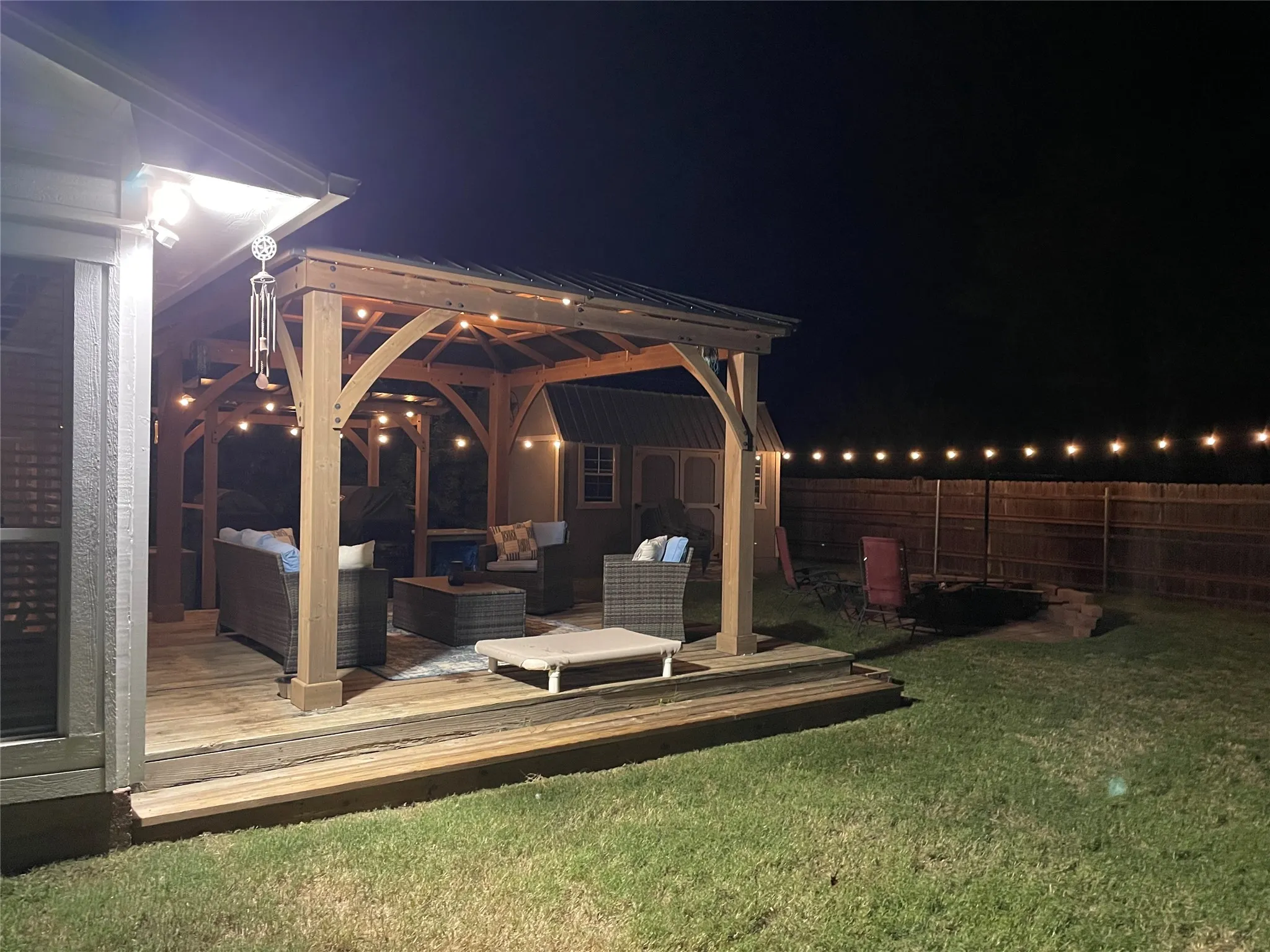 Wood-finish deck with a built-in pergola featuring string lighting, a manicured lawn, and a privacy fence