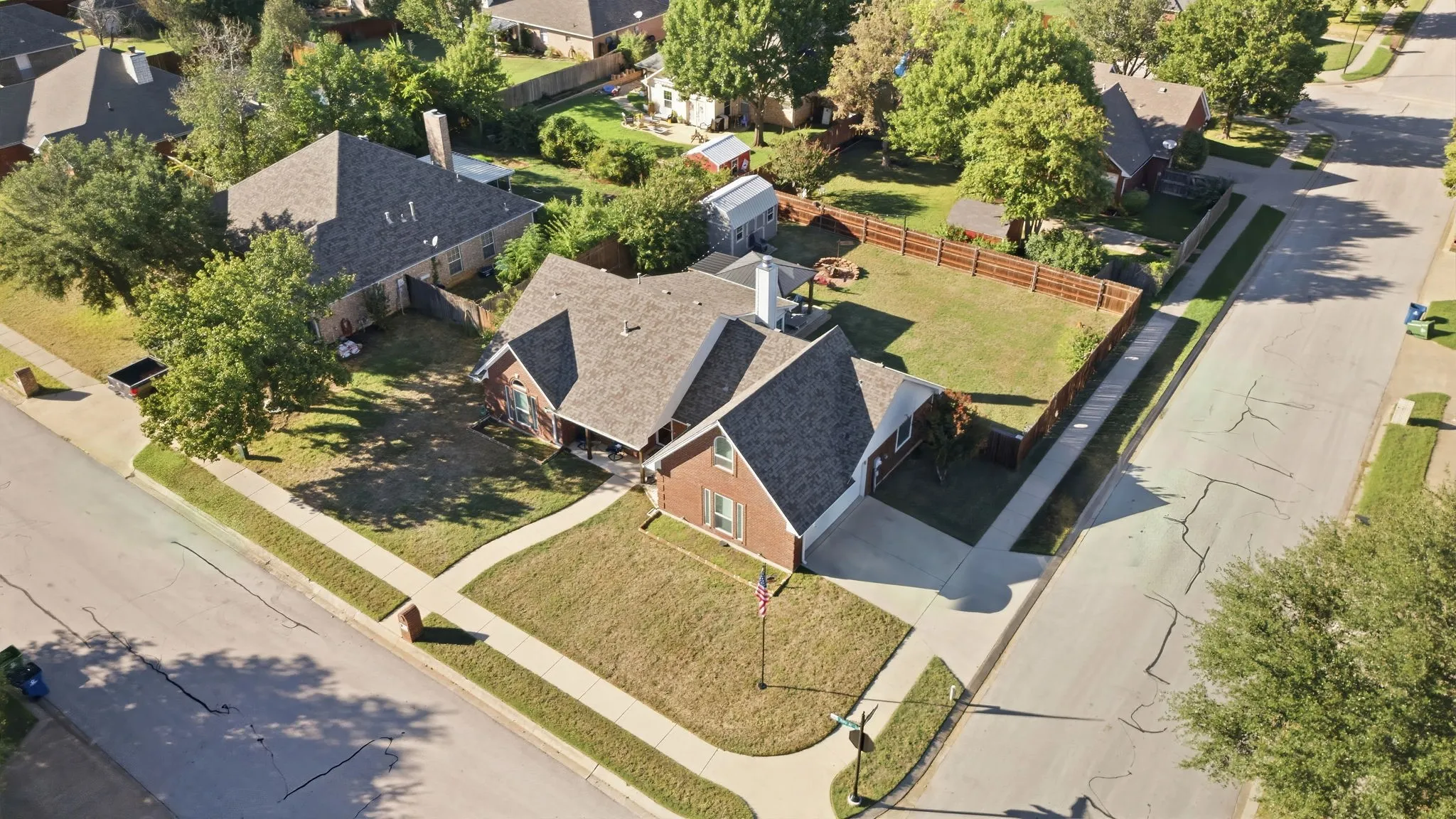 Brick exterior home with an attached garage, fenced backyard, and mature trees