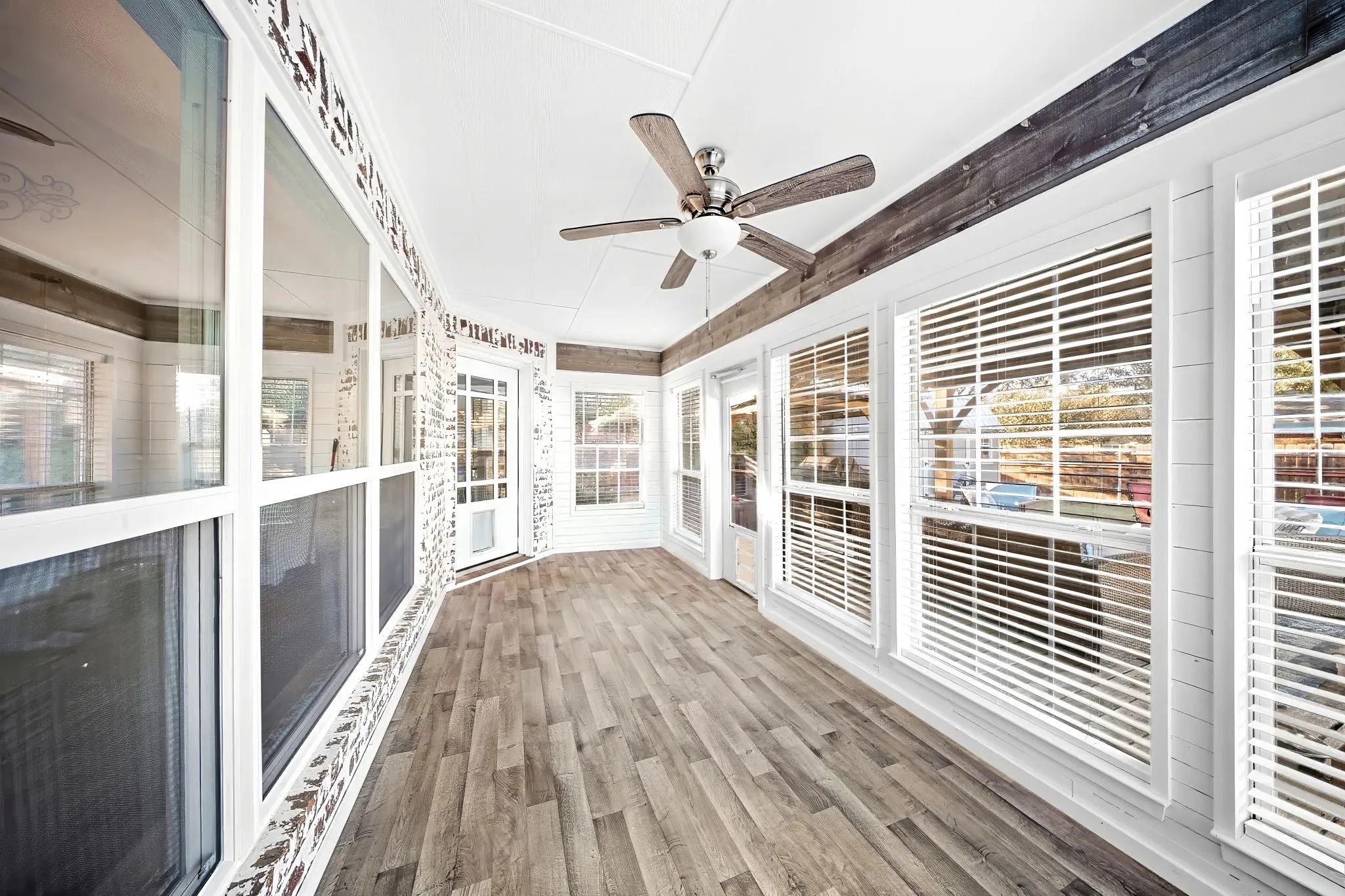 Enclosed porch featuring wood-finish flooring, white paneled walls, multiple windows with blinds, and a ceiling fan with light fixture