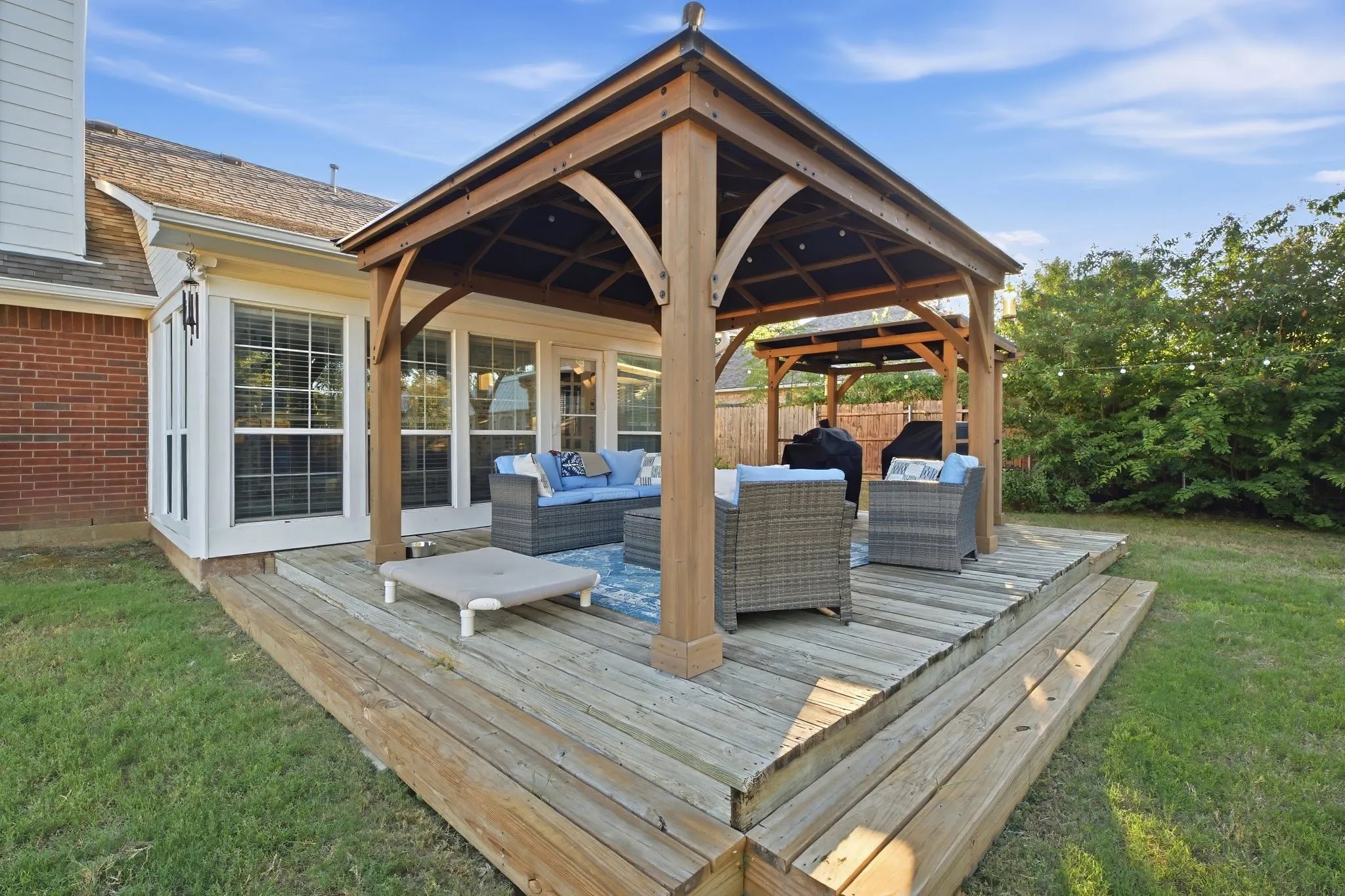Expansive wooden deck with two integrated gazebos, accessible via French doors, featuring a brick exterior