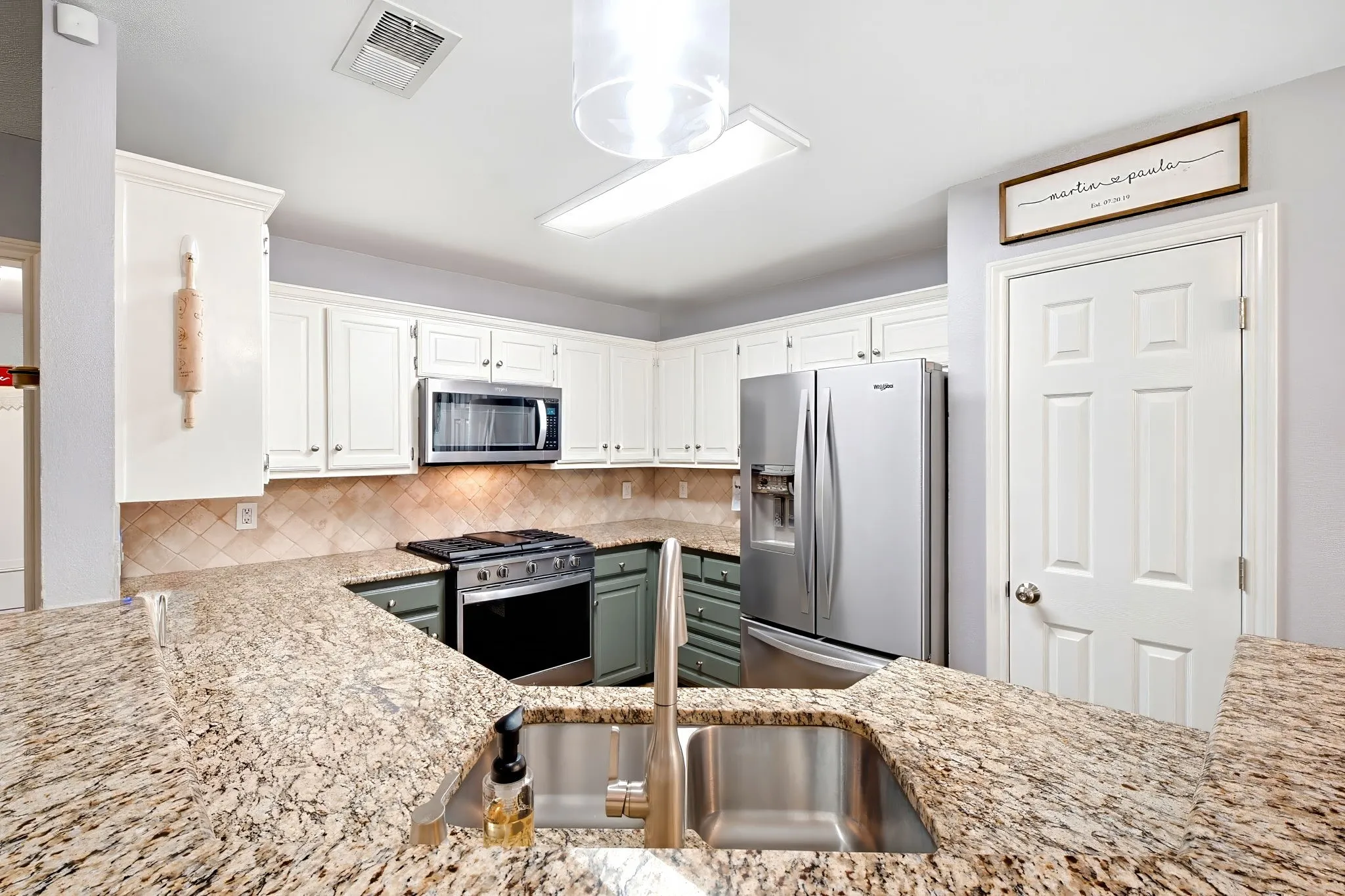 Granite countertops, stainless steel appliances, white upper cabinetry, and a tile backsplash