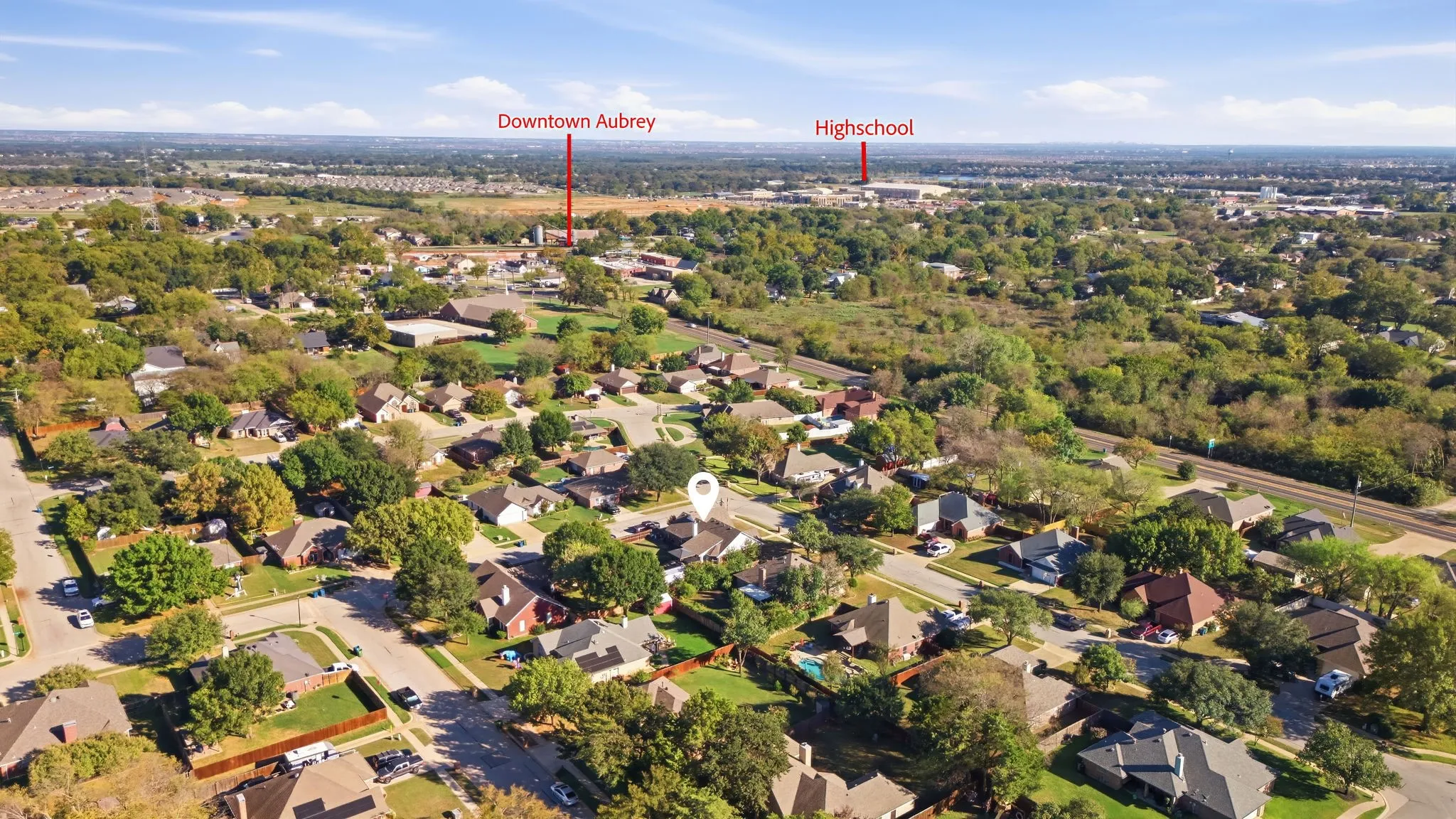 Aerial perspective of the surrounding area featuring residential streets, mature trees, and a distant commercial building
