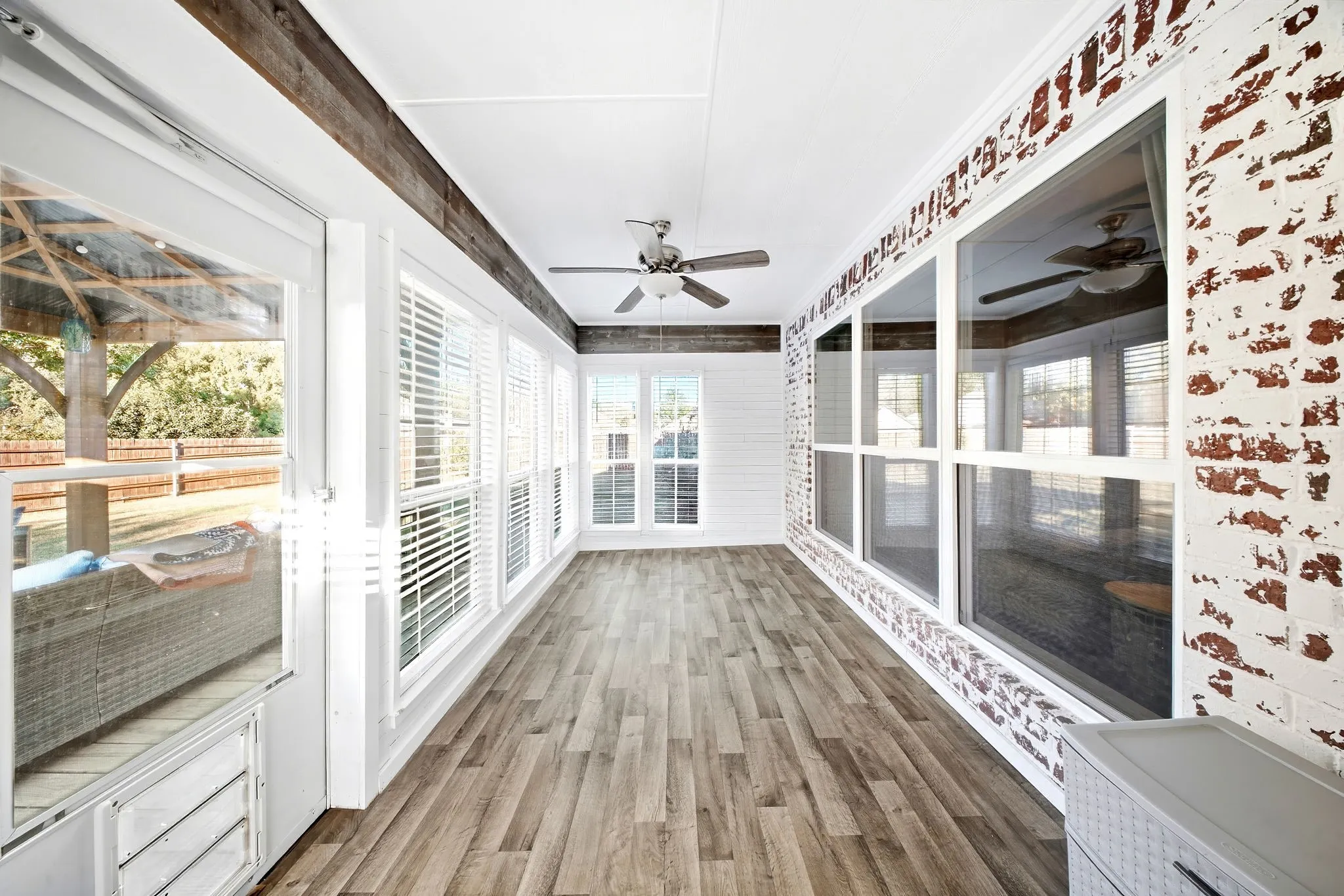 Enclosed sunroom featuring multiple large windows, wood-finish flooring, a ceiling fan, and exposed brick accents