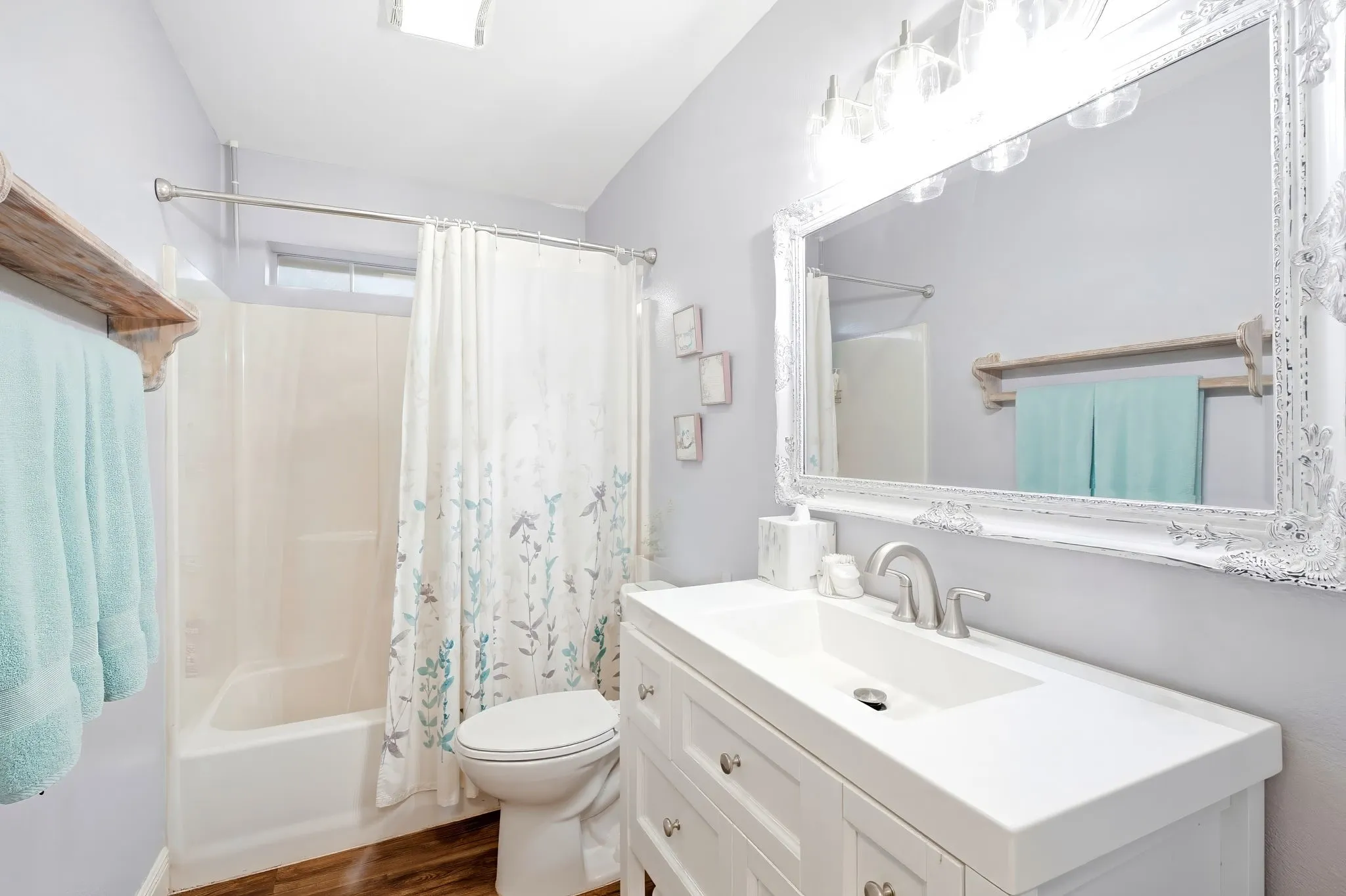 White vanity with integrated sink, brushed nickel faucet, large ornate framed mirror, and wood-finish flooring