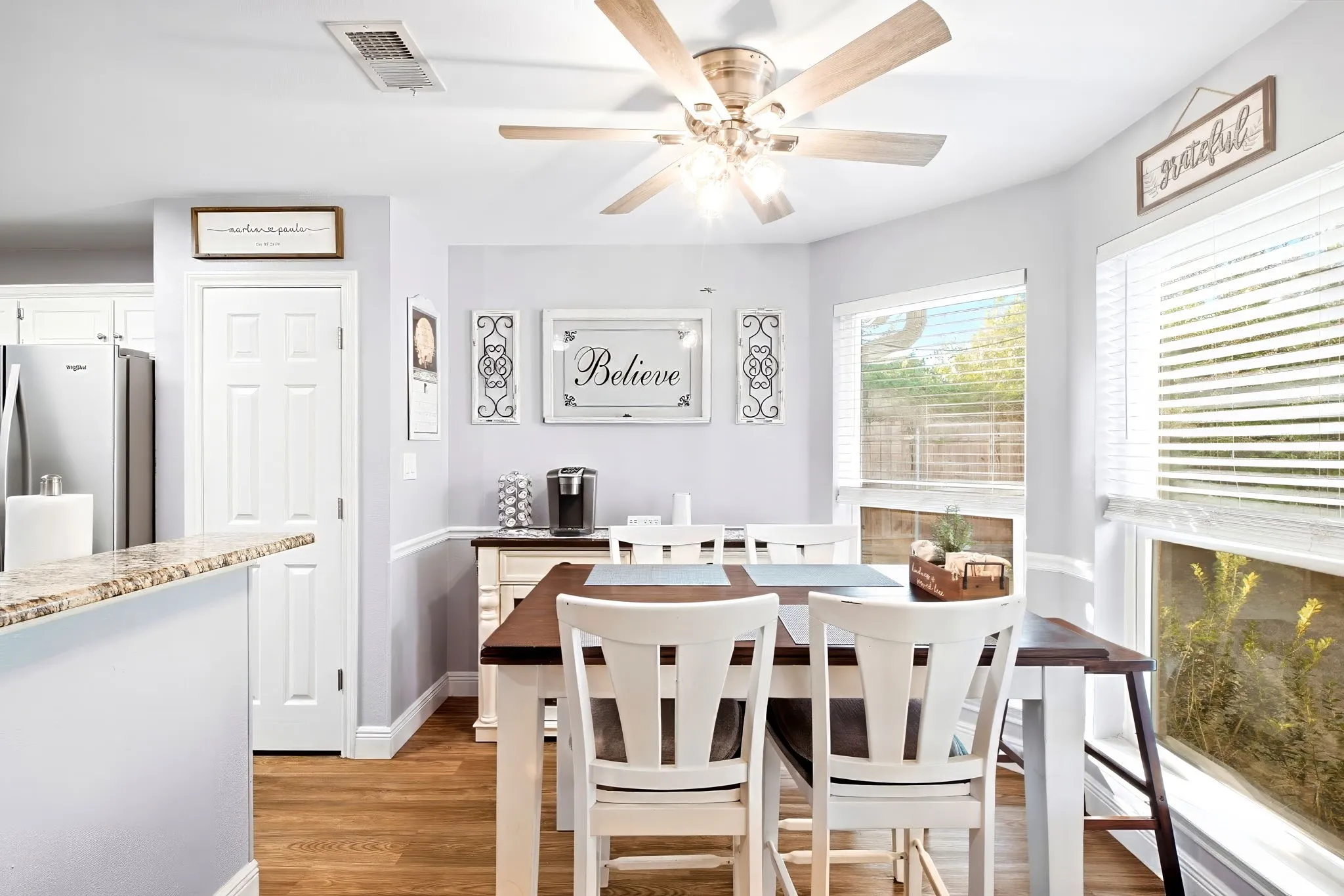 Open-concept dining area featuring wood-finish flooring, a ceiling fan with integrated lighting, and multiple windows with blinds