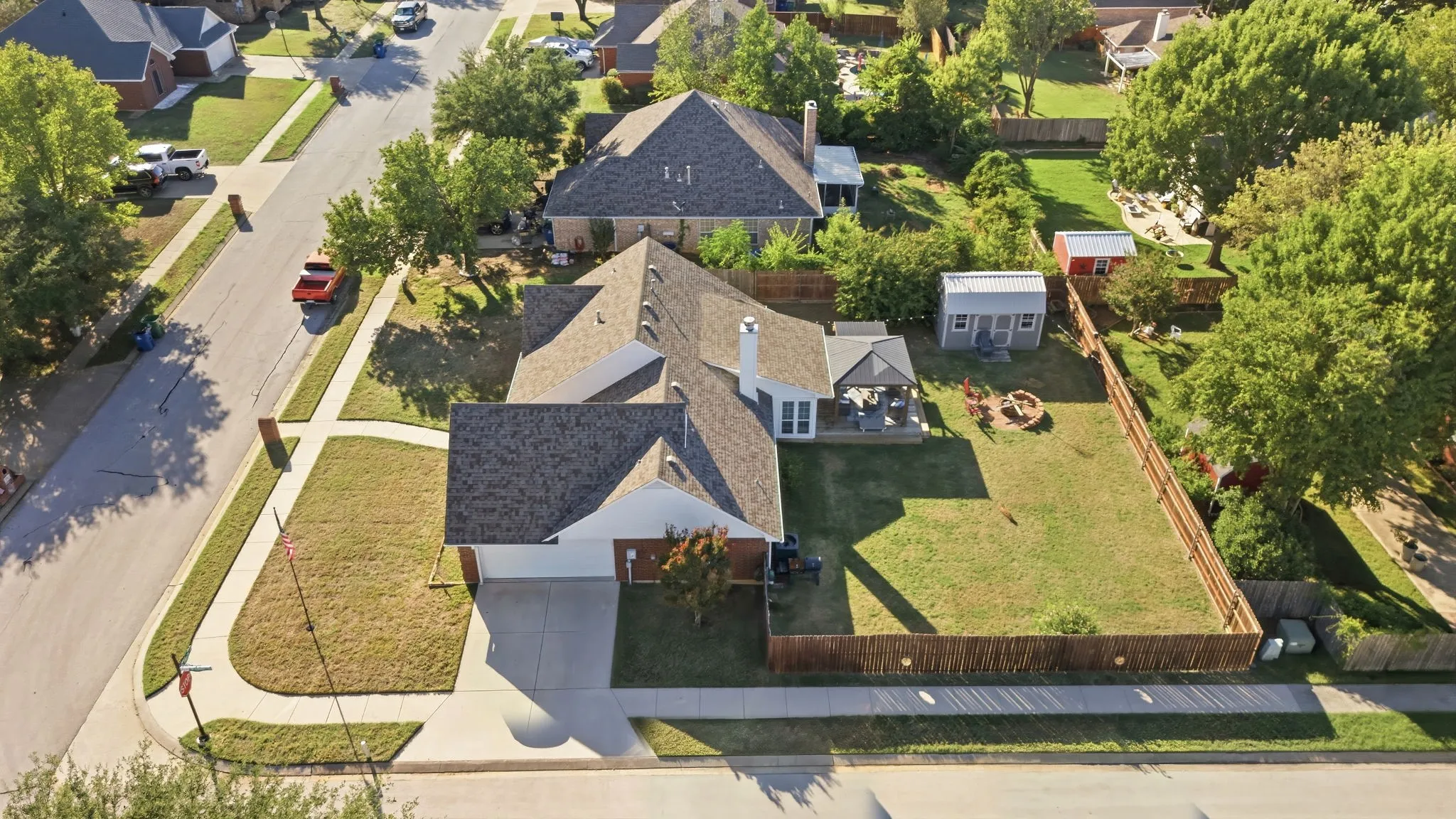 Expansive fenced backyard featuring a fire pit, mature trees, and a detached storage shed