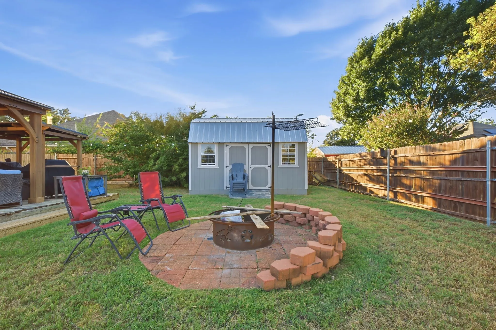 Expansive backyard featuring a fire pit with a paver base, a wooden privacy fence, a storage shed, and a covered patio structure