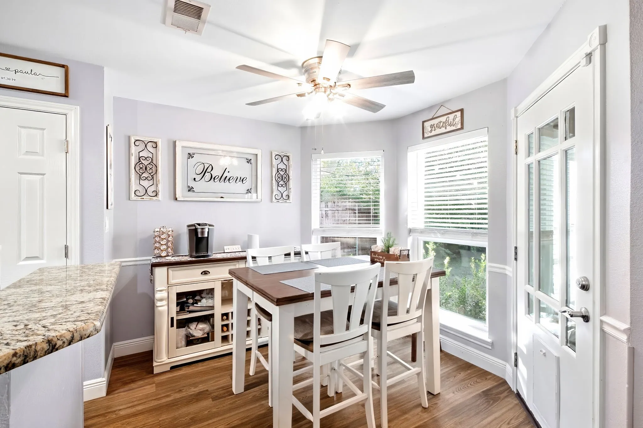 Wood-finish flooring, granite countertop, multiple windows with blinds, ceiling fan, and a transom door