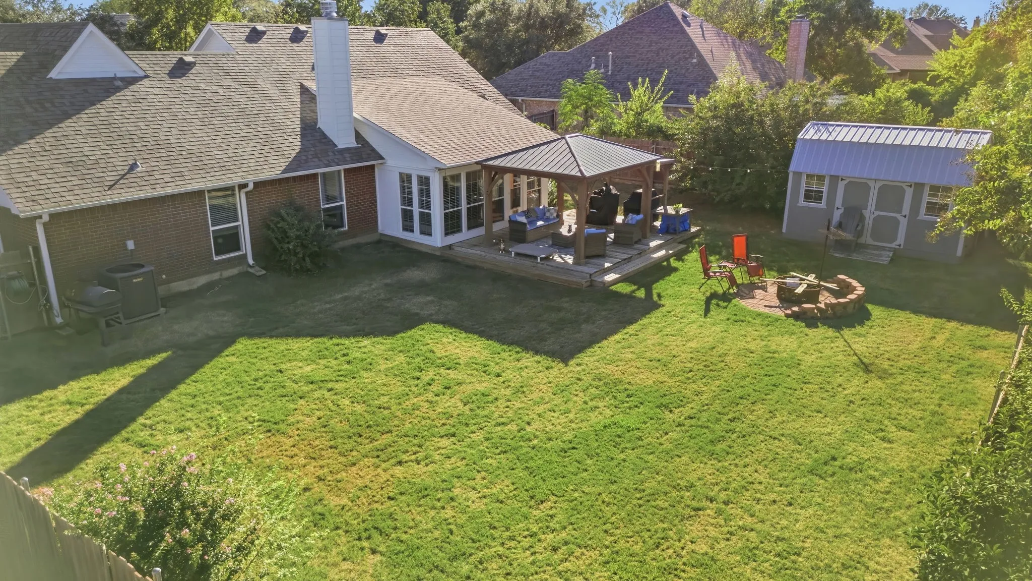 Expansive backyard featuring a large lawn, a wooden deck with a gazebo, a stone fire pit area, and a storage shed