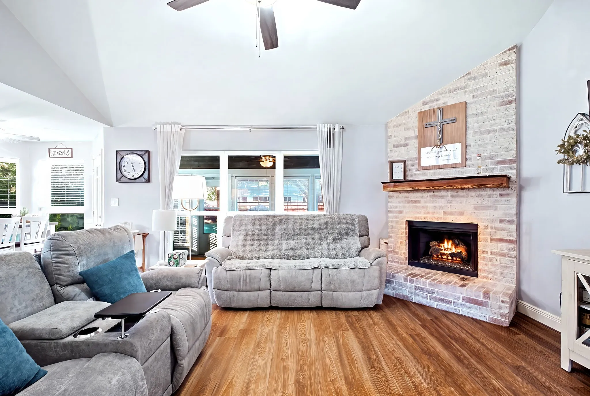 Vaulted ceiling, wood-finish flooring, brick fireplace with a wood mantel, and expansive windows