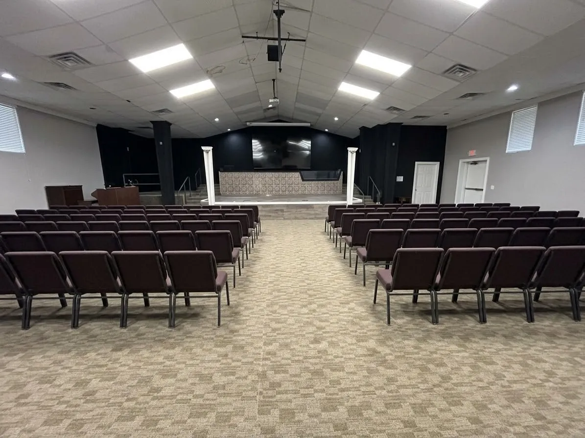 Large open space with patterned carpet flooring, stage with decorative columns, and recessed lighting