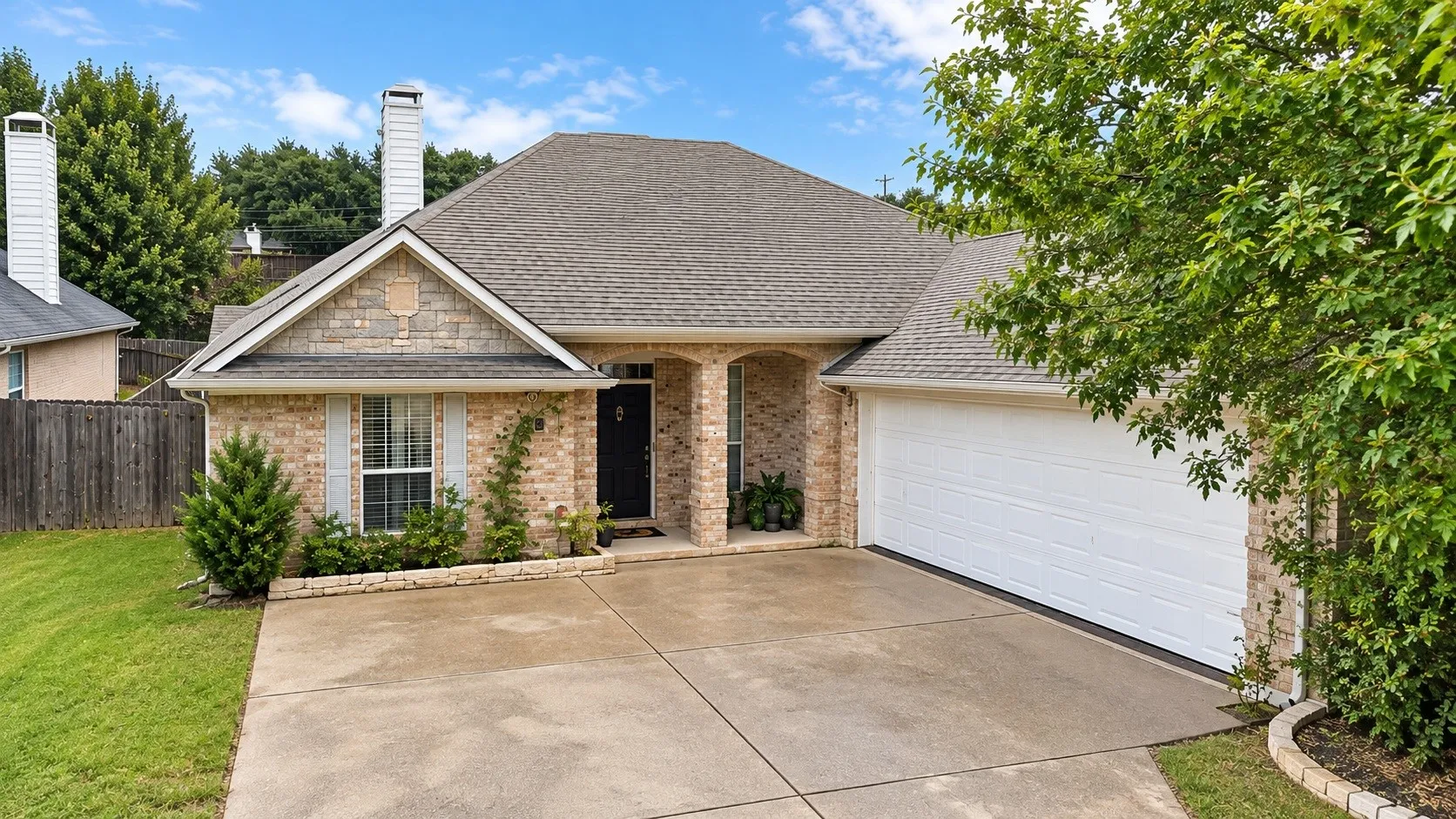 Brick facade with stone accents, a concrete driveway, an attached garage, a covered entryway, and a shingled roof