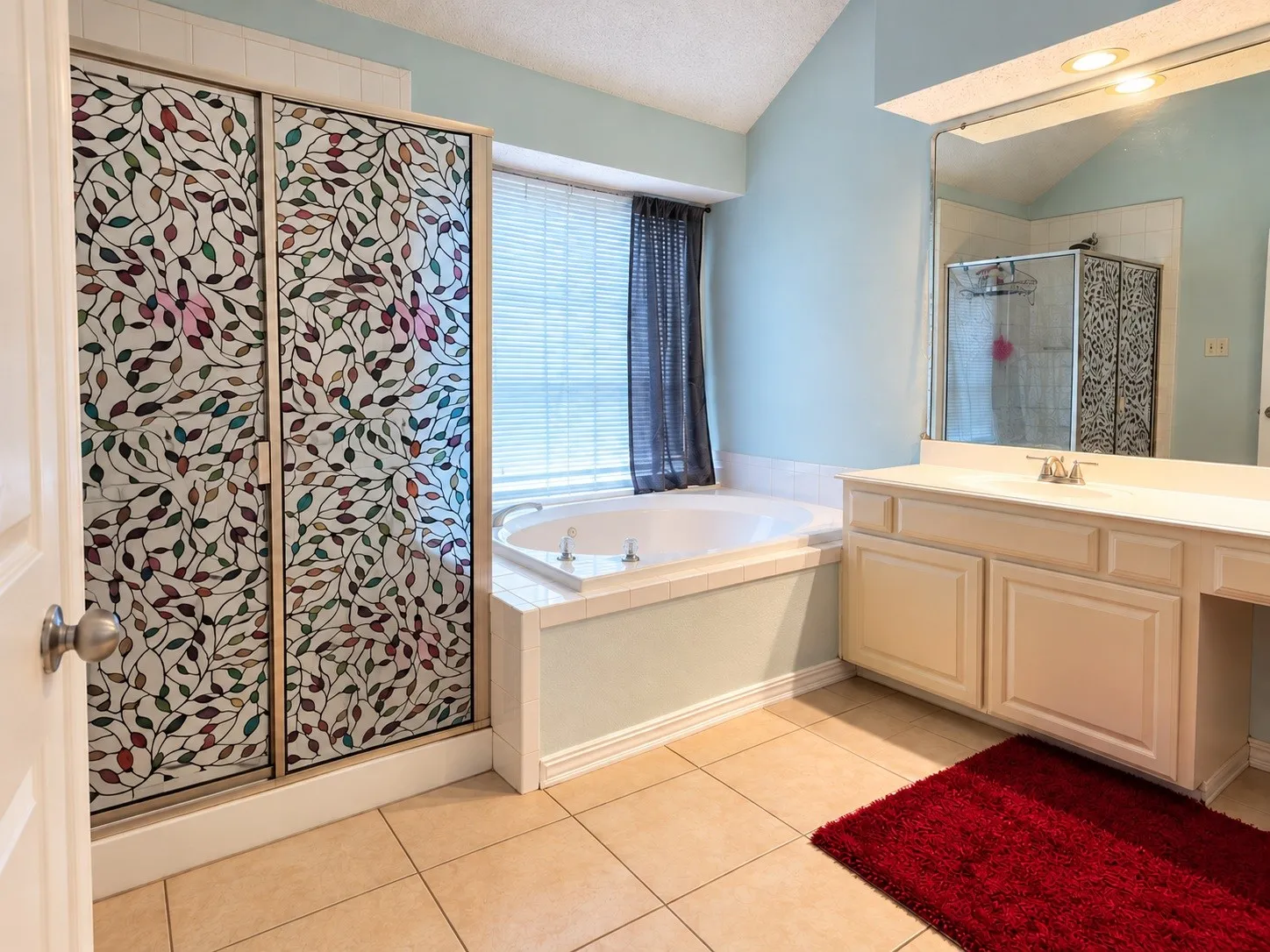Recessed lighting, tile flooring, built-in vanity with integrated sink, soaking tub, and vaulted ceiling