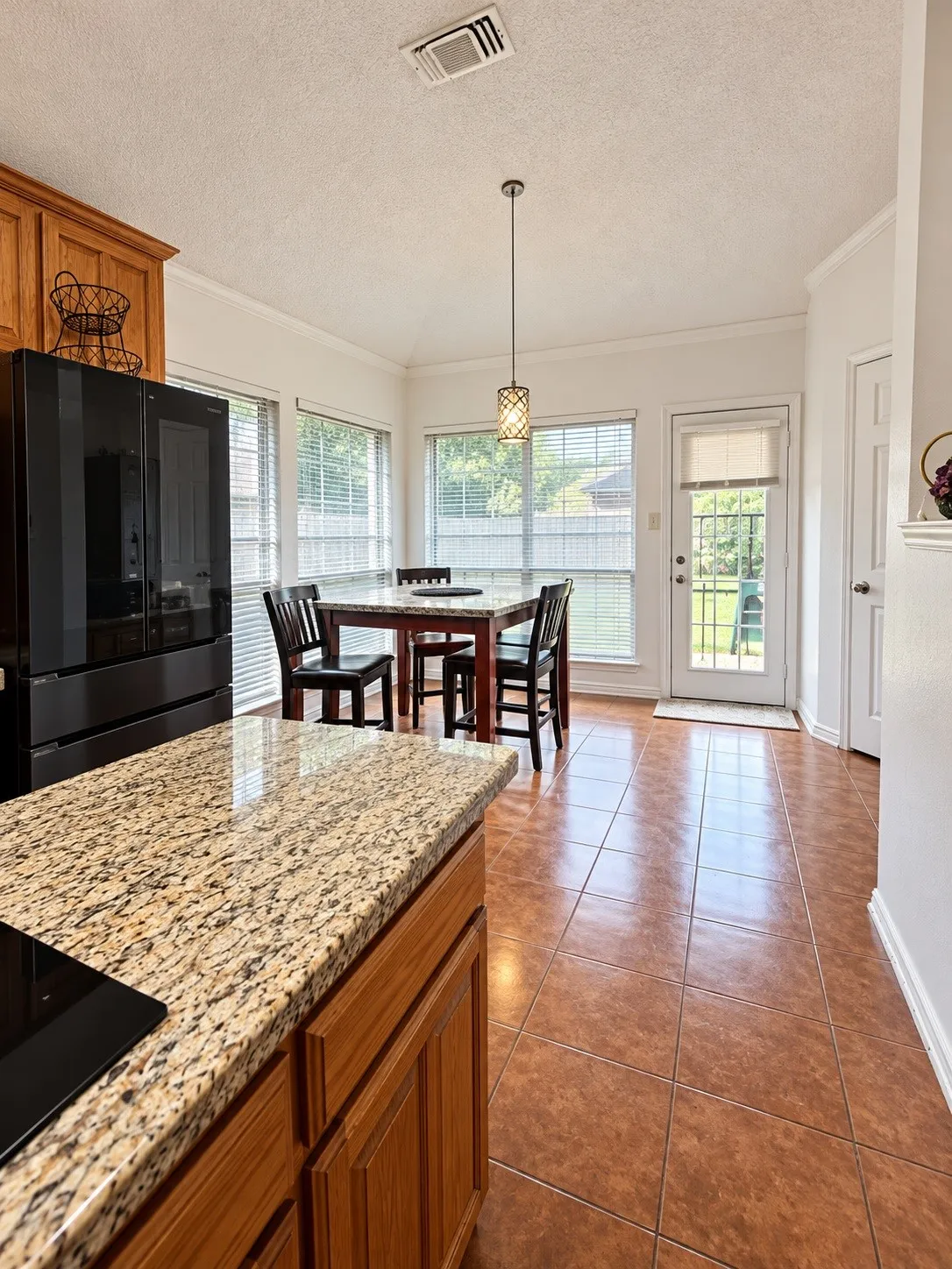 Kitchen featuring granite countertops, wood cabinetry, tile flooring, and a pendant light fixture