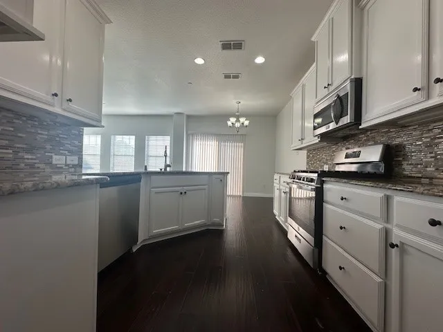Kitchen featuring white cabinetry, stone countertops, stainless steel appliances, a mosaic tile backsplash, and dark wood-finish flooring