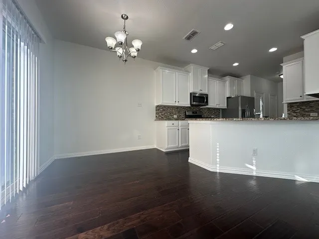 Open-concept kitchen and dining area featuring dark wood-finish flooring, white cabinetry, integrated stainless steel appliances, a tiled backsplash, and recessed lighting