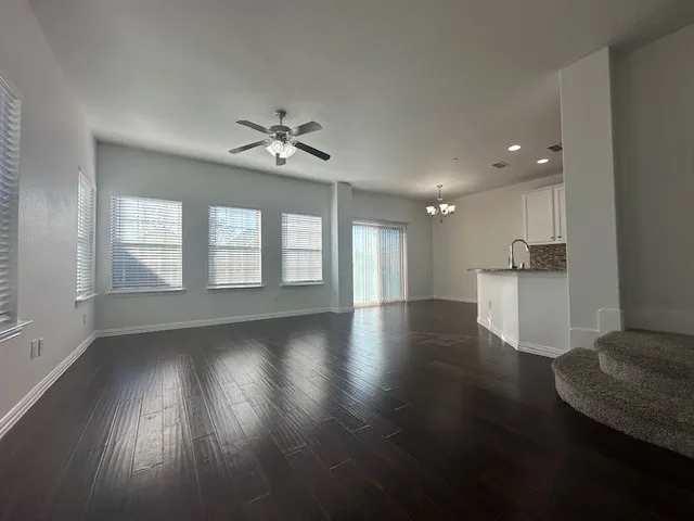 Spacious open-concept living area featuring wood-finish flooring, multiple windows with blinds, and a ceiling fan