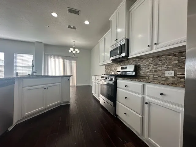 Kitchen featuring white cabinetry, stainless steel appliances, mosaic tile backsplash, and dark wood-finish flooring