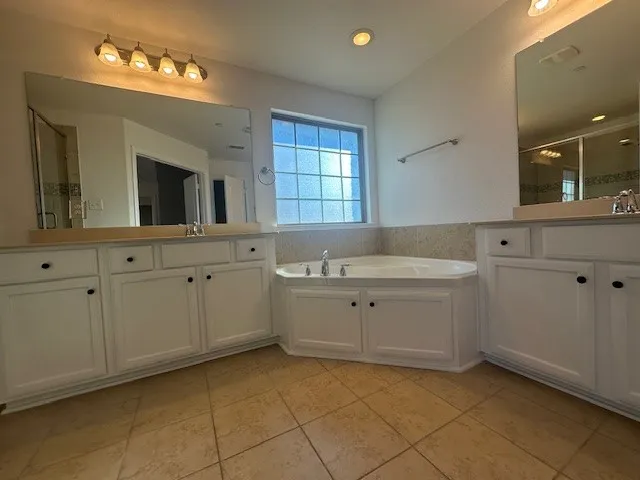 Corner soaking tub, dual vanities with integrated sinks, recessed lighting, and tile flooring