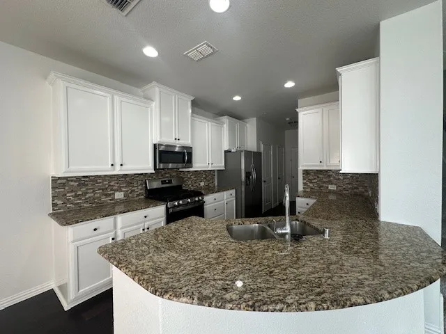 Kitchen featuring white cabinetry, stainless steel appliances, mosaic tile backsplash, and a large breakfast bar with a double basin sink
