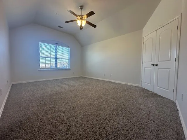 Vaulted ceiling with a ceiling fan, arched window with horizontal blinds, and a neutral carpeted floor