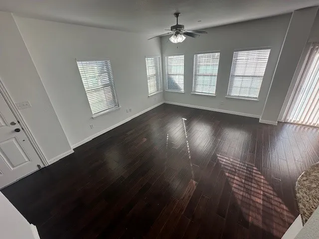 Spacious room with dark wood-finish flooring, multiple windows, and a ceiling fan with integrated lighting