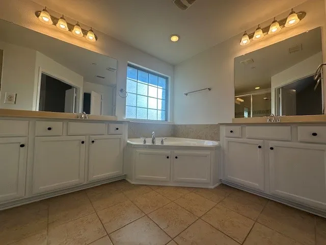 Dual vanities with white cabinetry, a built-in corner tub, and tiled flooring