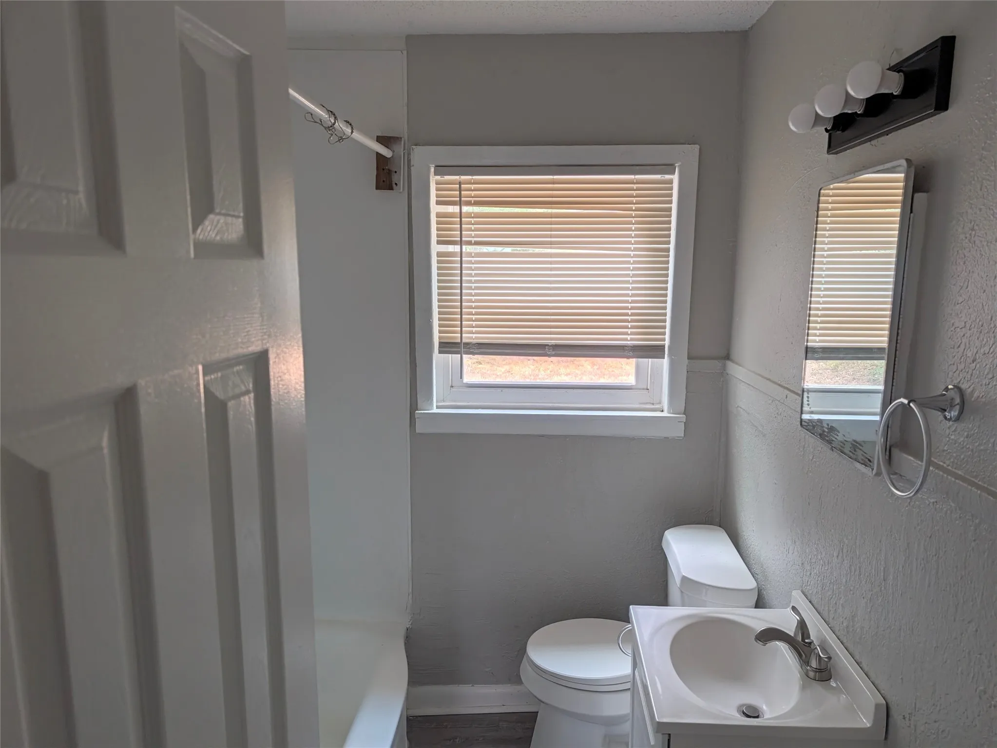 White panel door, window with blinds, vanity sink, mirror, and wall-mounted light fixture
